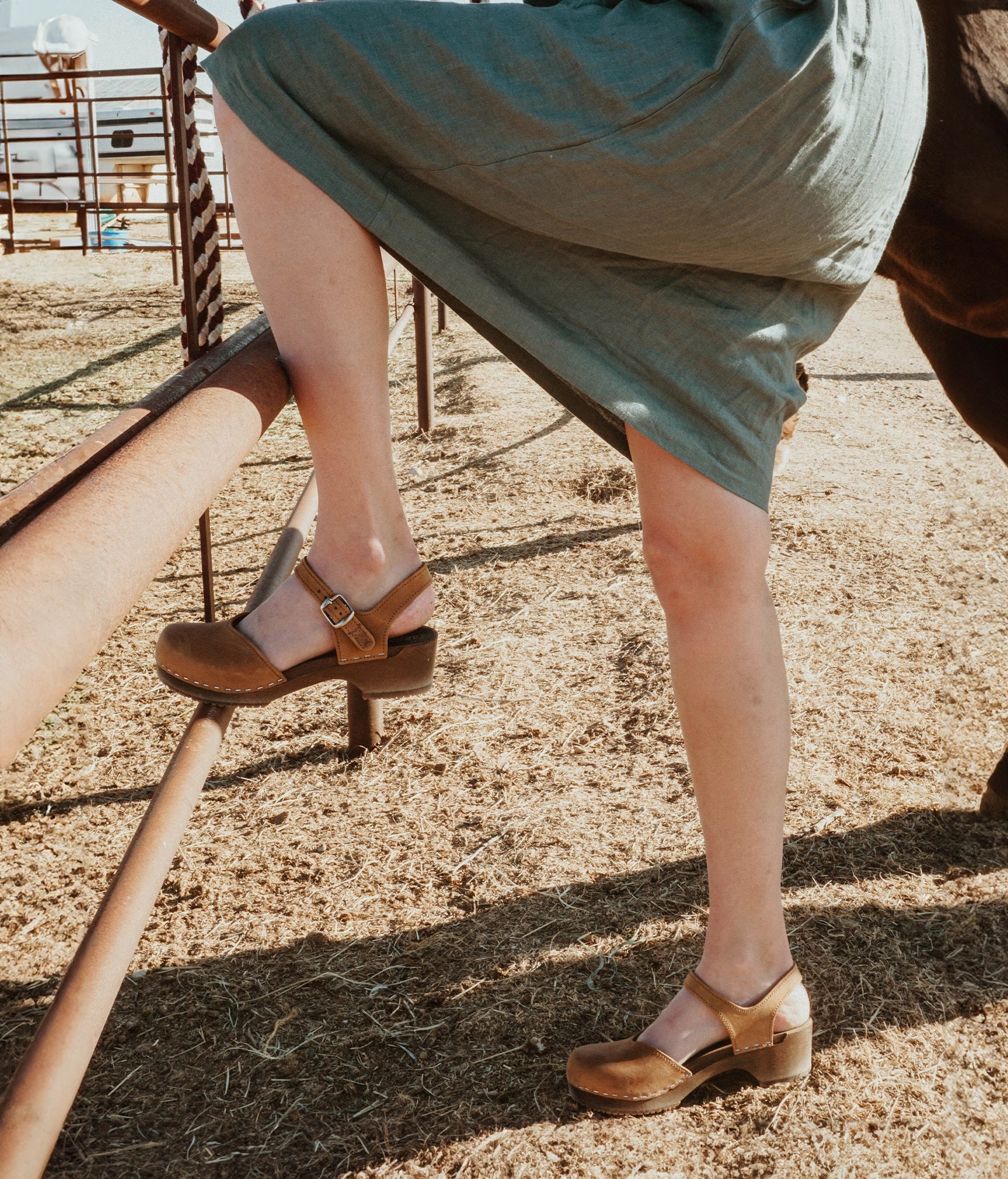 classic low heeled closed-toe sandal in light brown nubuck leather stapled on a dark wooden base