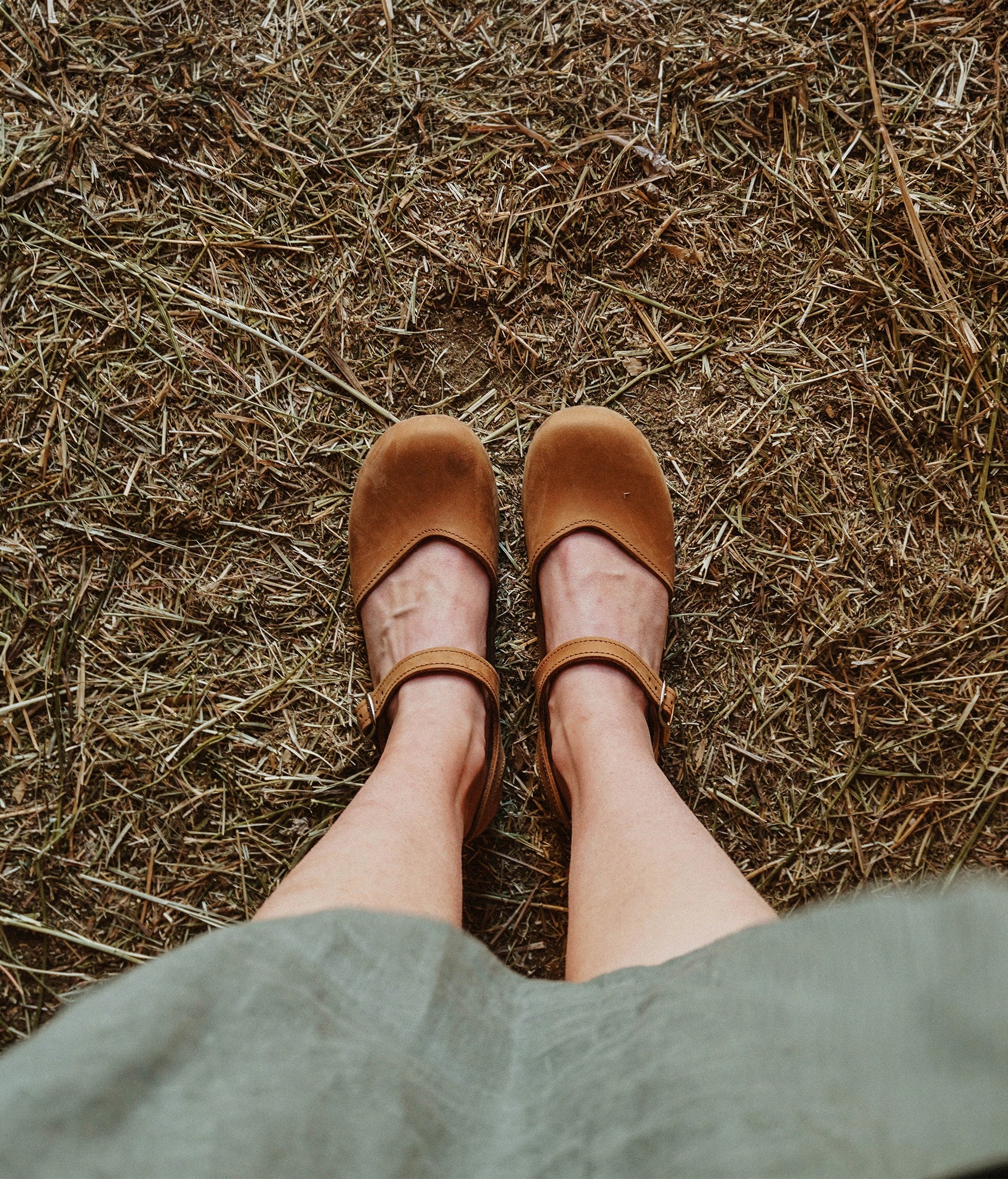 classic low heeled closed-toe sandal in light brown nubuck leather stapled on a dark wooden base