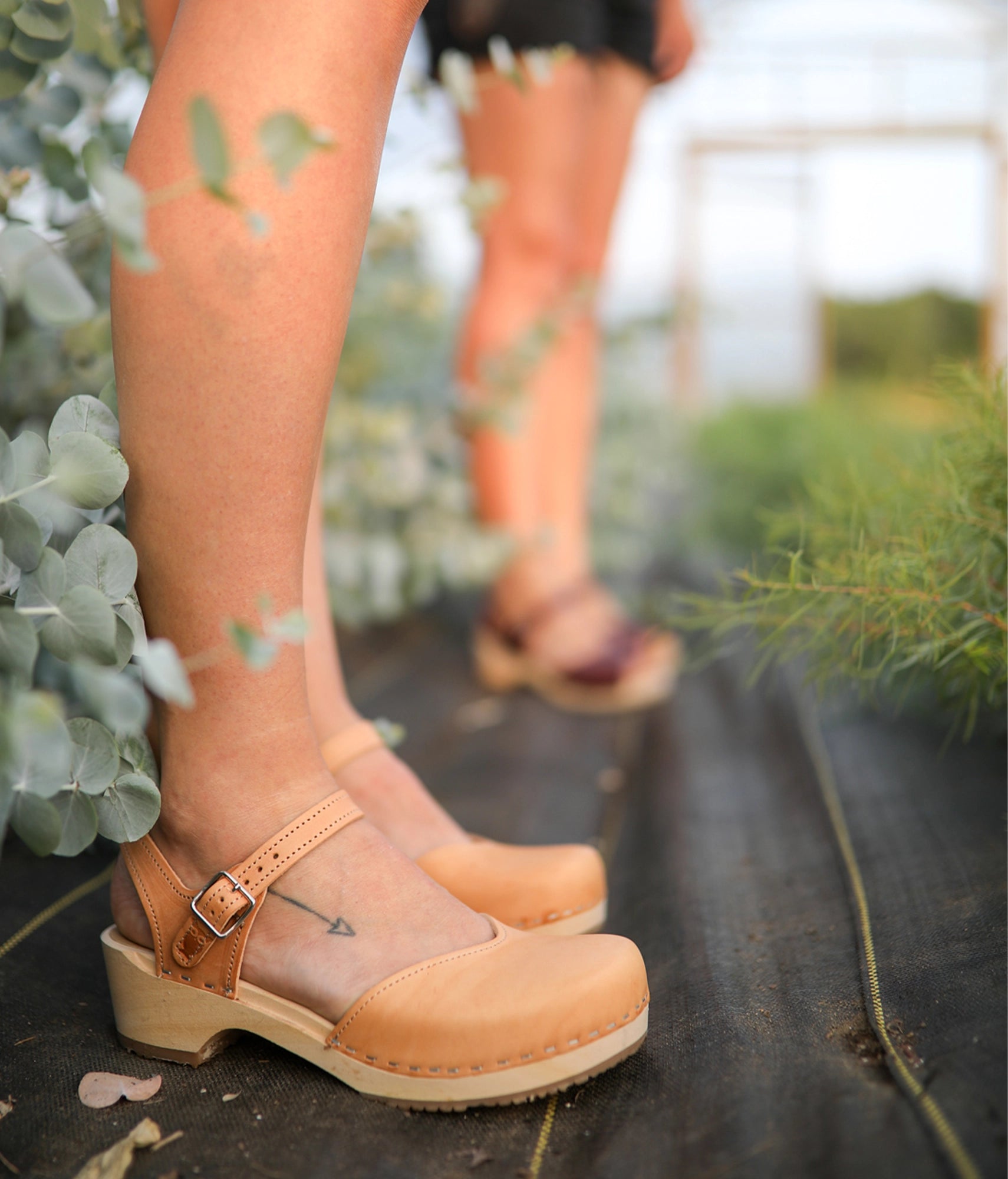 Woman wearingclassic low heeled closed-toe sandal in ecru beige vegetable tanned leather stapled on a light wooden base