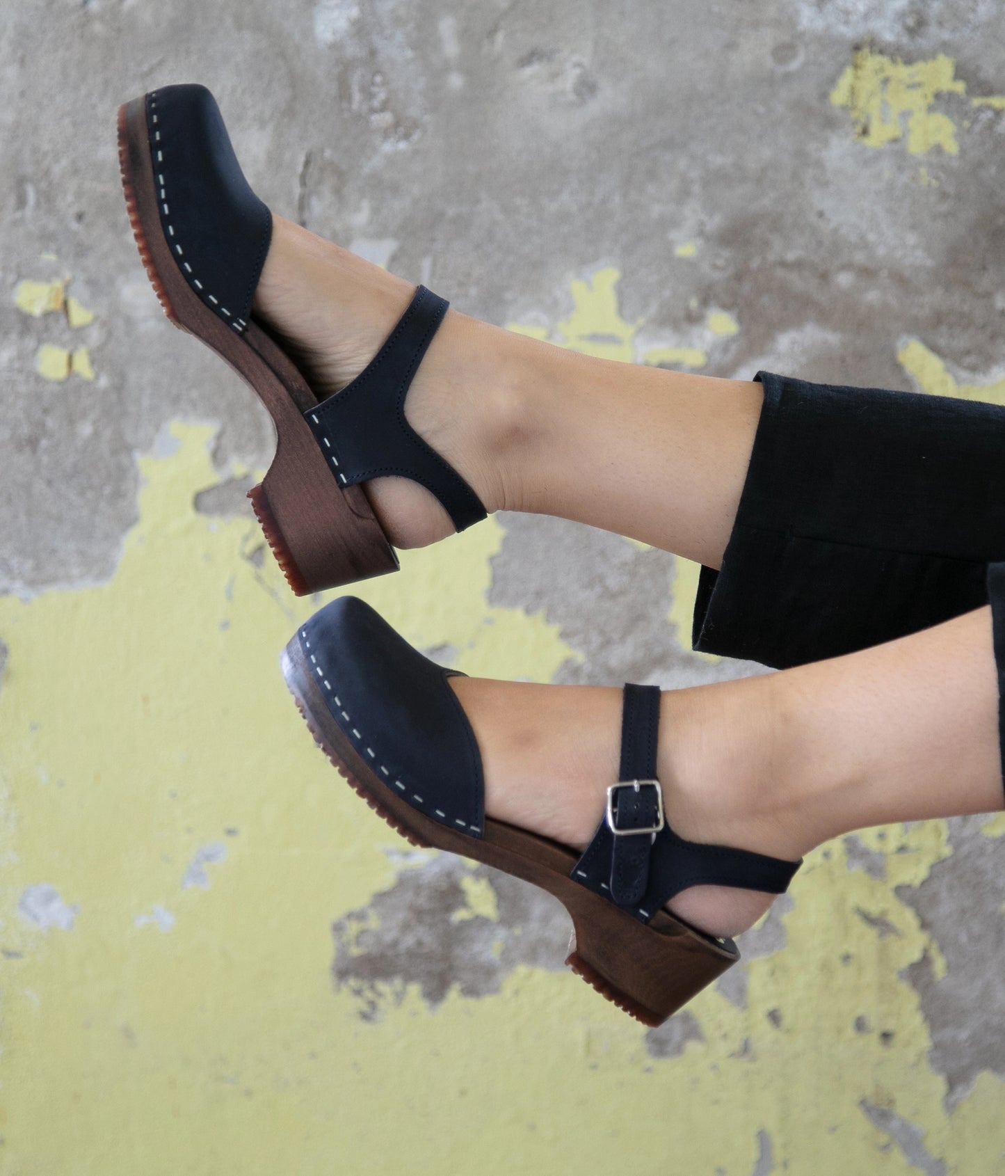 Woman wearing classic low heeled closed-toe sandal in navy blue nubuck leather stapled on a dark wooden base