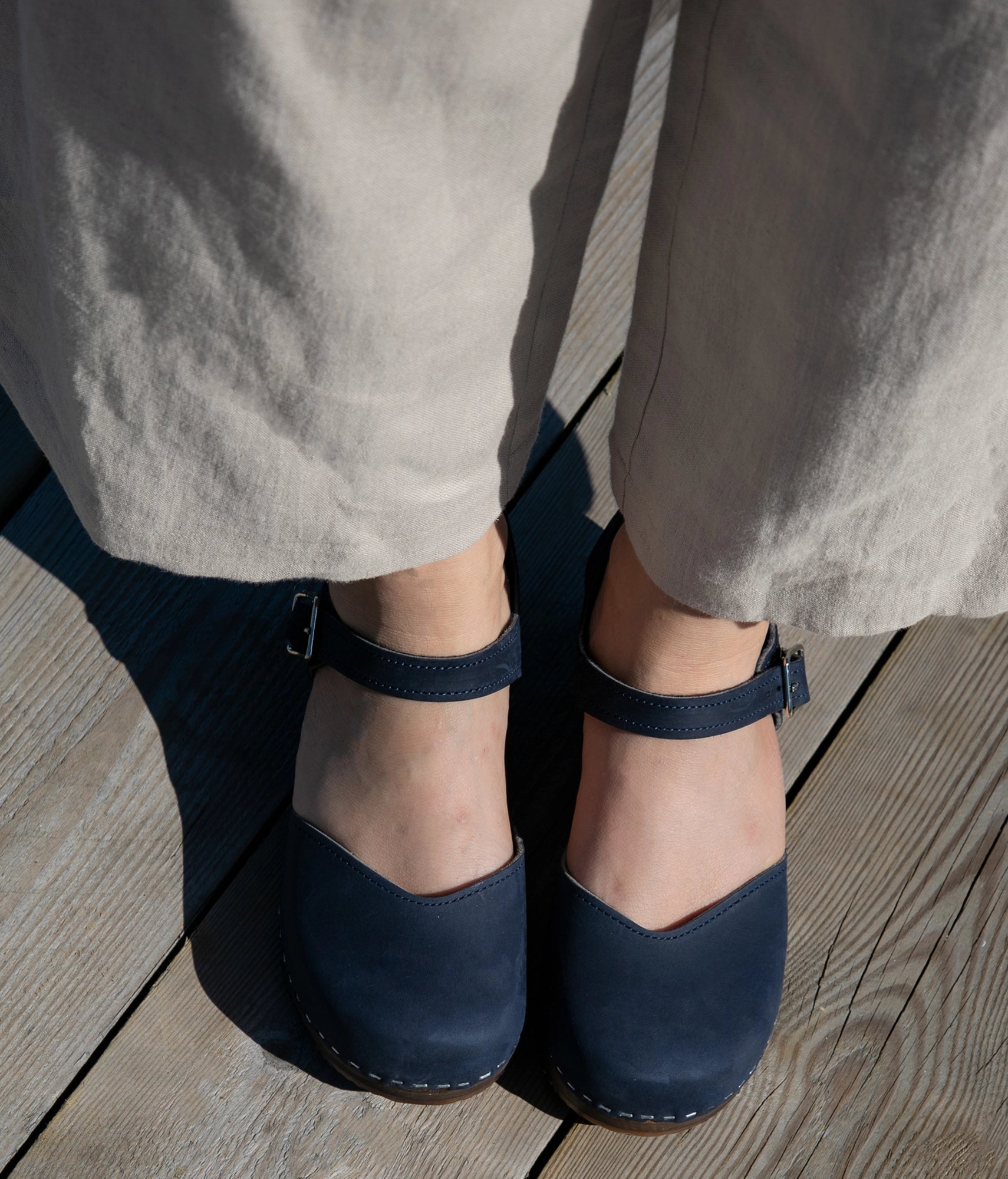 classic low heeled closed-toe sandal in navy blue nubuck leather stapled on a dark wooden base