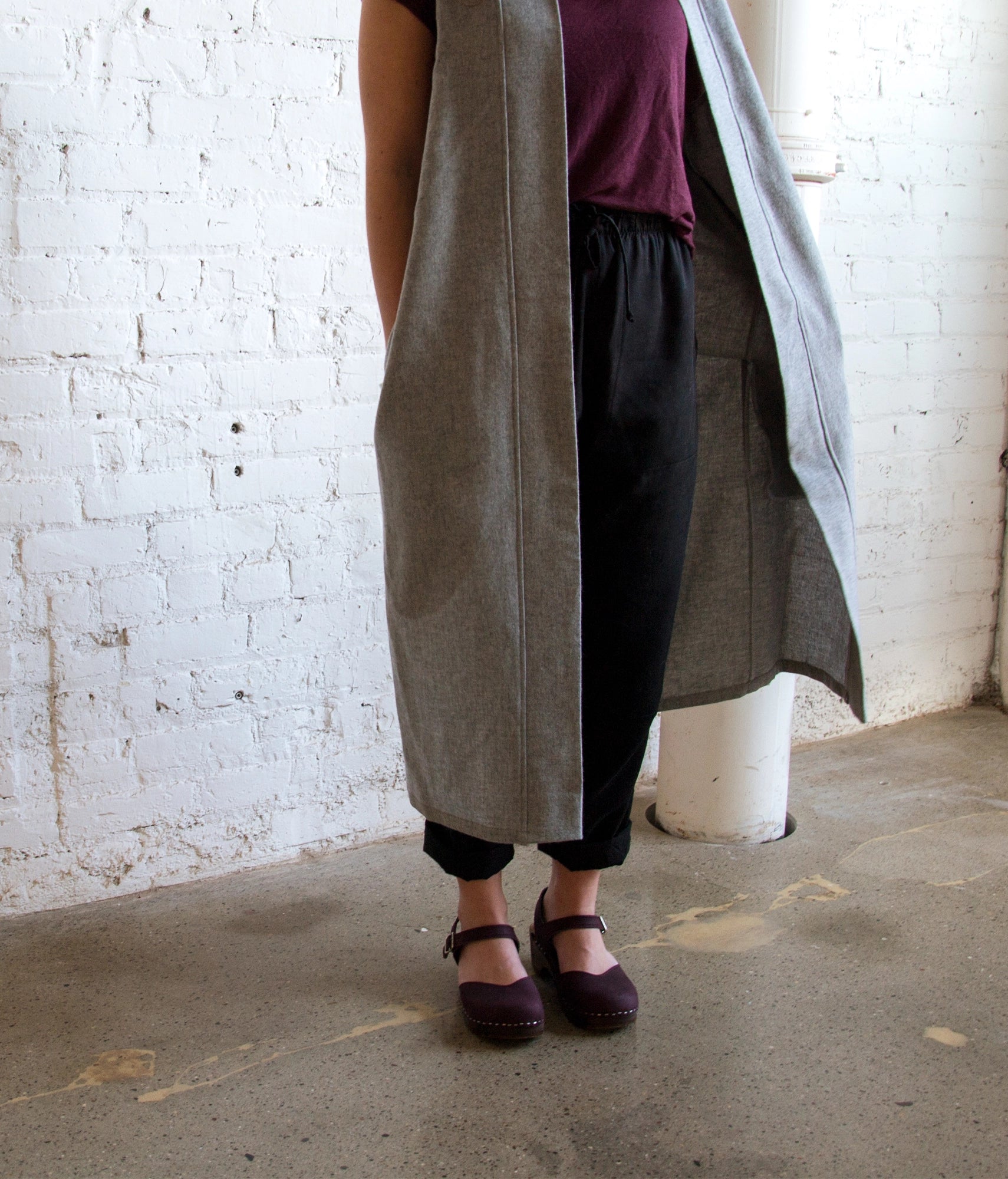 Woman wearing classic low heeled closed-toe sandal in purple plum nubuck leather stapled on a dark wooden base