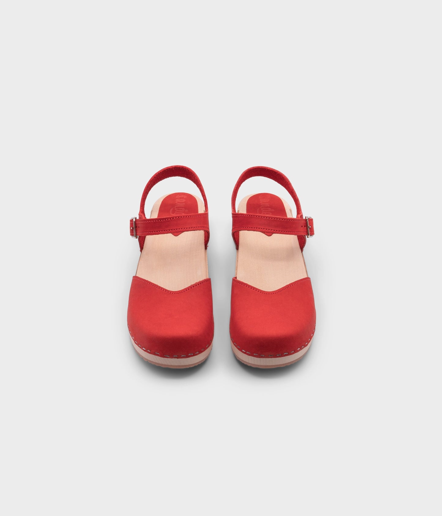 classic low heeled closed-toe sandal in red nubuck leather stapled on a light wooden base