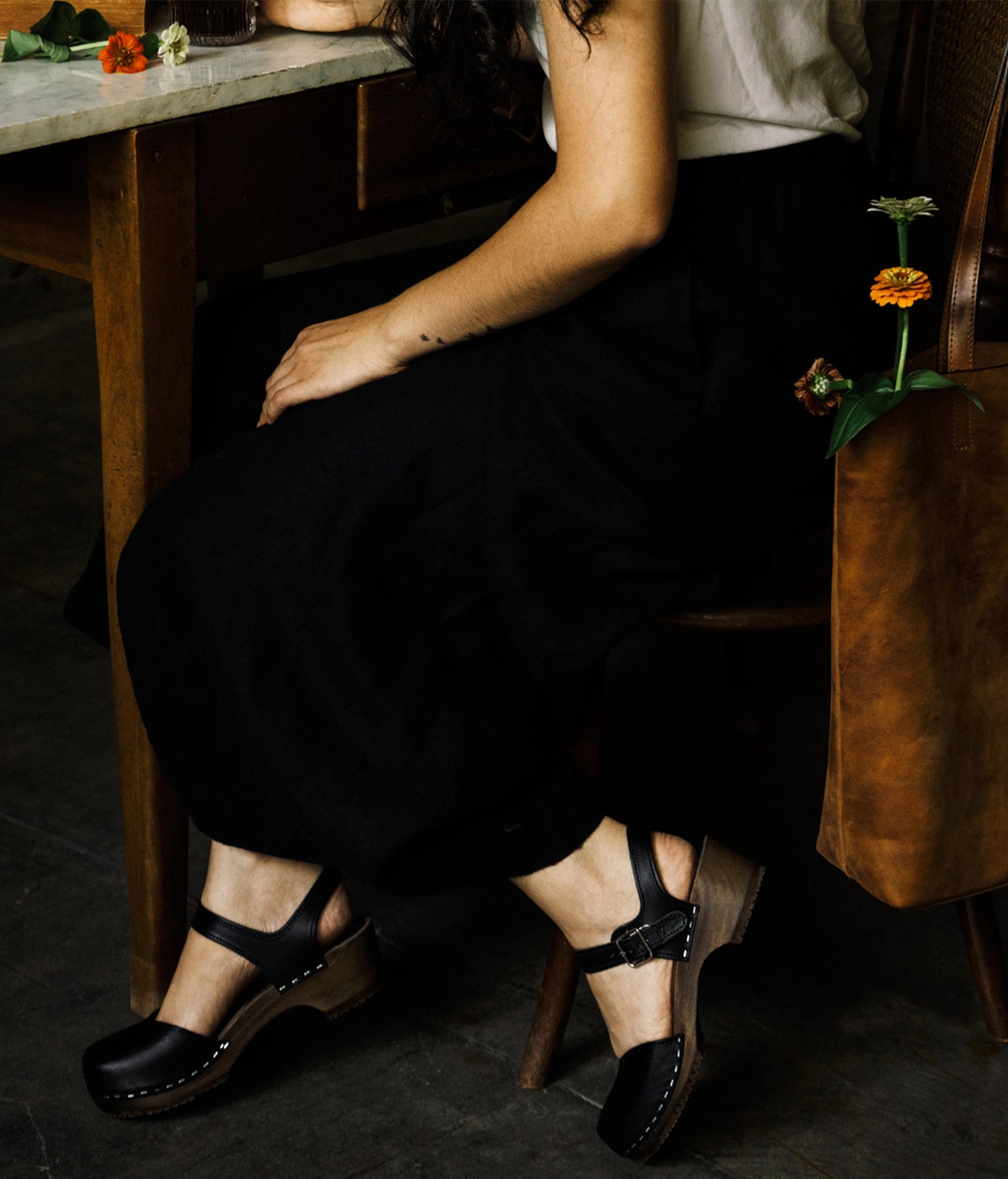 Women wearing classic low heeled closed-toe sandal in black vegetable tanned leather stapled on a dark wooden base