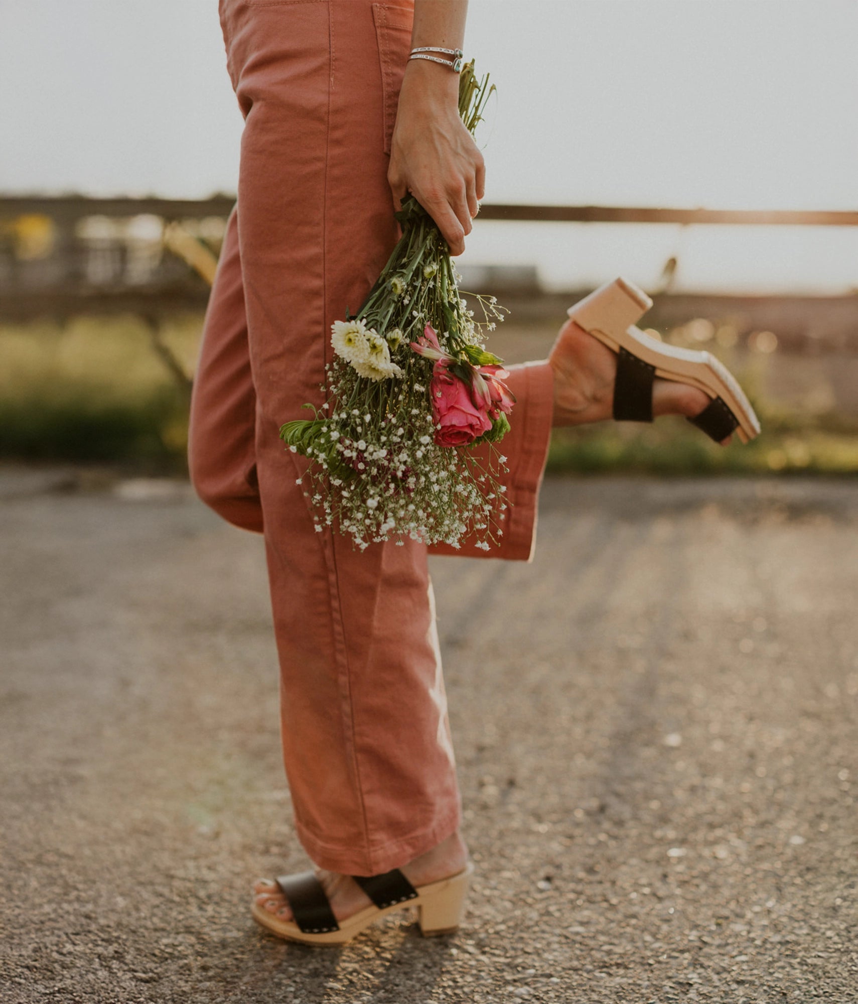 Woman in high heeled slip-in clog sandal with open toe in black vegetable tanned leather stapled on a light wooden base