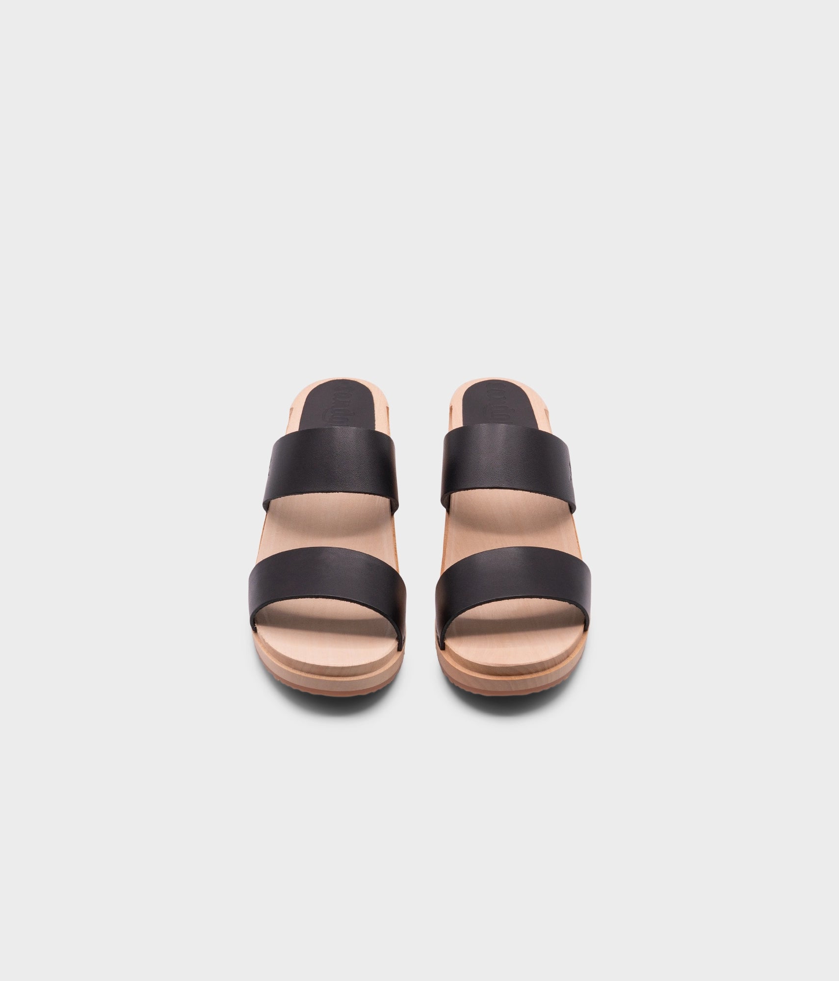 low heeled slip-in clog sandal with open toe in black vegetable tanned leather stapled on a light wooden base