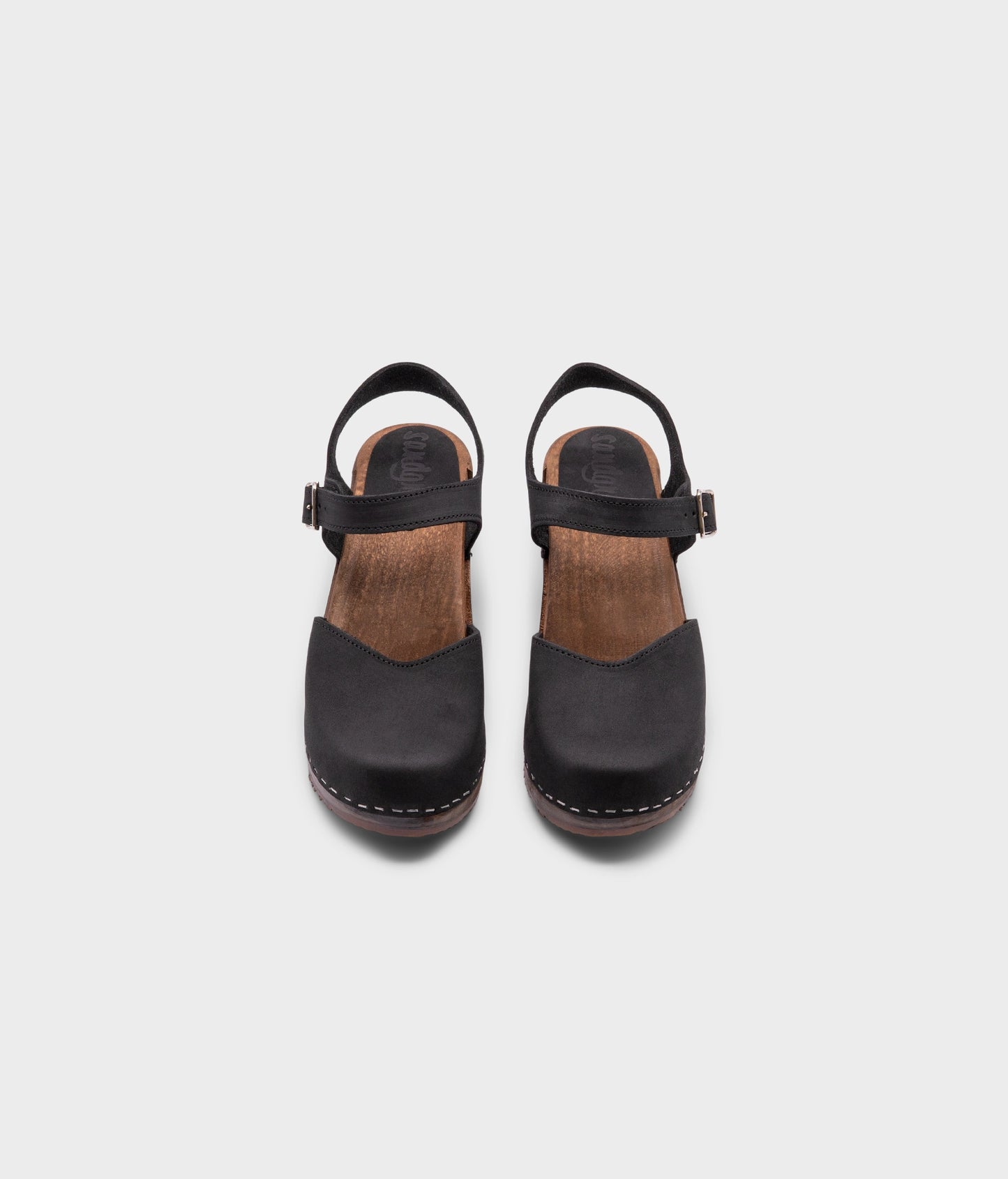 high heeled closed-toe clog sandal in black nubuck leather stapled on a dark wooden base