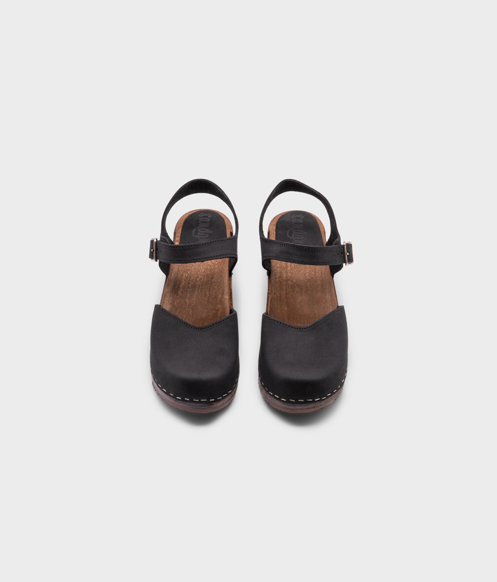 high heeled closed-toe clog sandal in black nubuck leather stapled on a dark wooden base