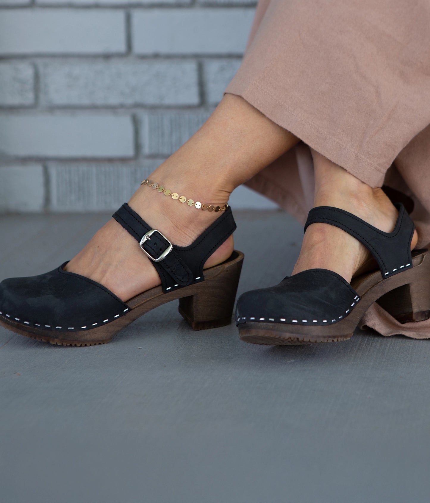 high heeled closed-toe clog sandal in black nubuck leather stapled on a dark wooden base