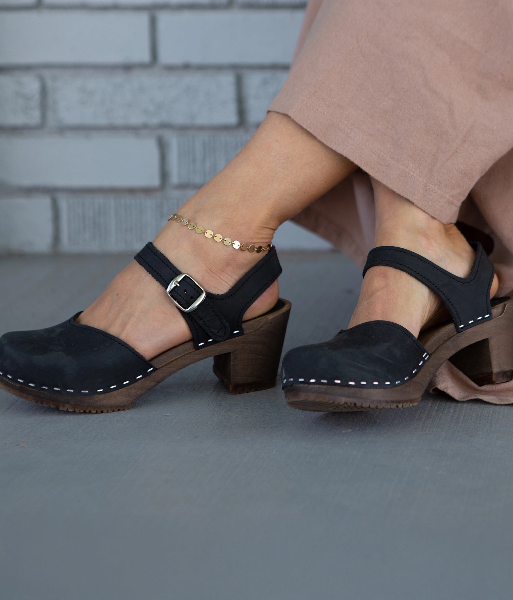 high heeled closed-toe clog sandal in black nubuck leather stapled on a dark wooden base