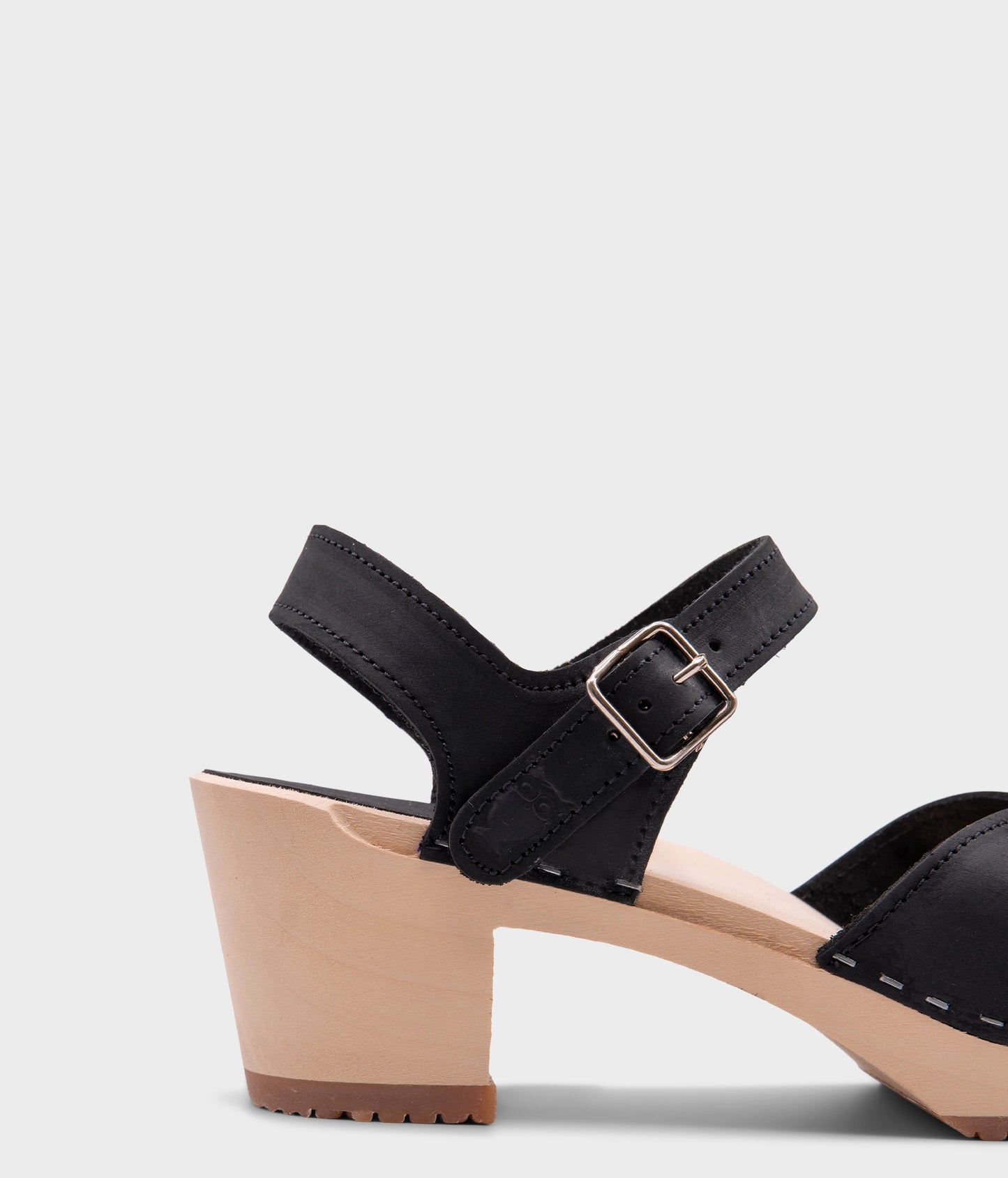 high heeled closed-toe clog sandal in black nubuck leather stapled on a light wooden base