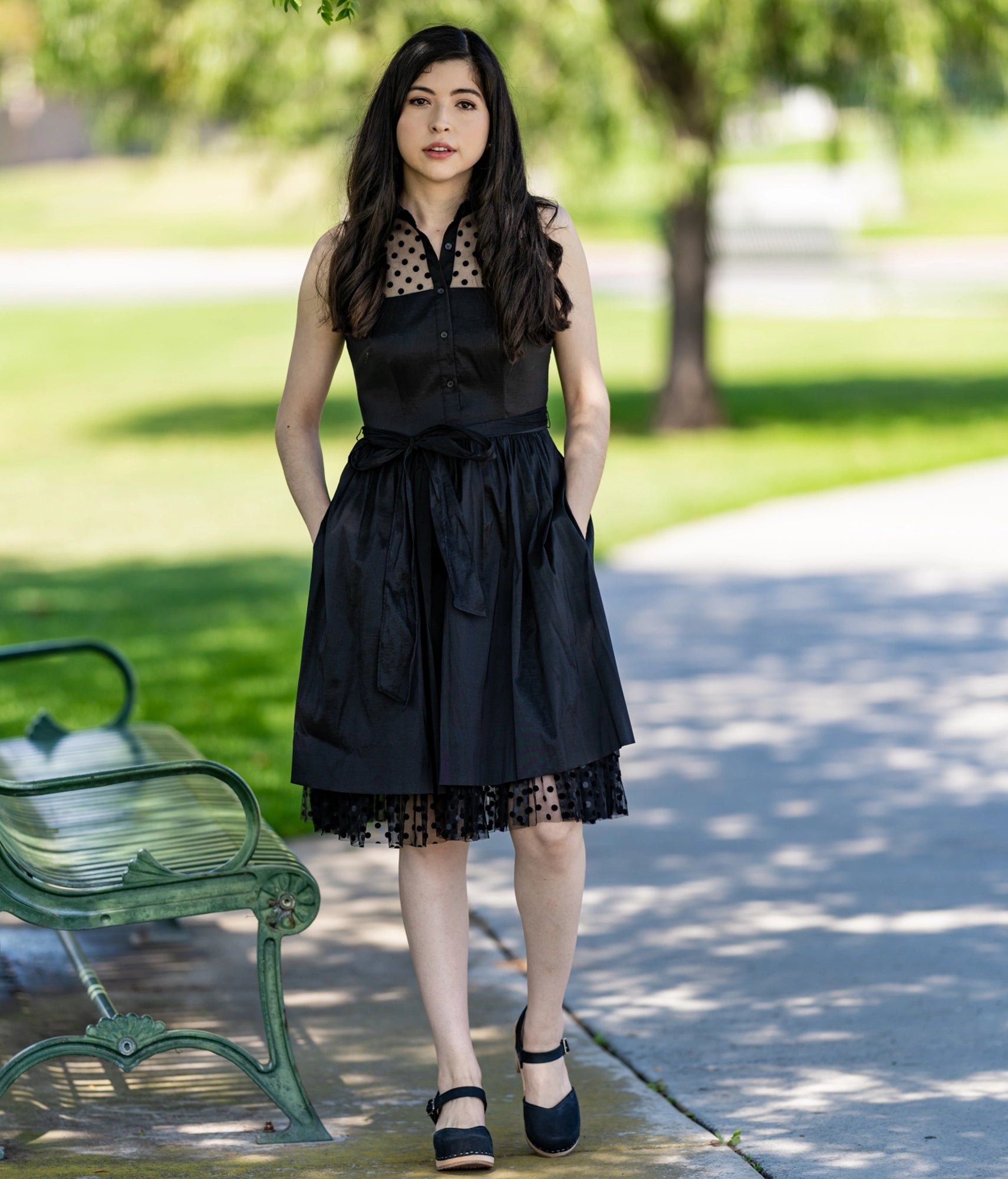 Woman wearing high heeled closed-toe clog sandal in black nubuck leather stapled on a light wooden base