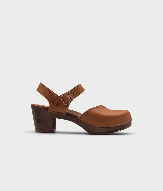 high heeled closed-toe clog sandal in light brown nubuck leather stapled on a dark wooden base