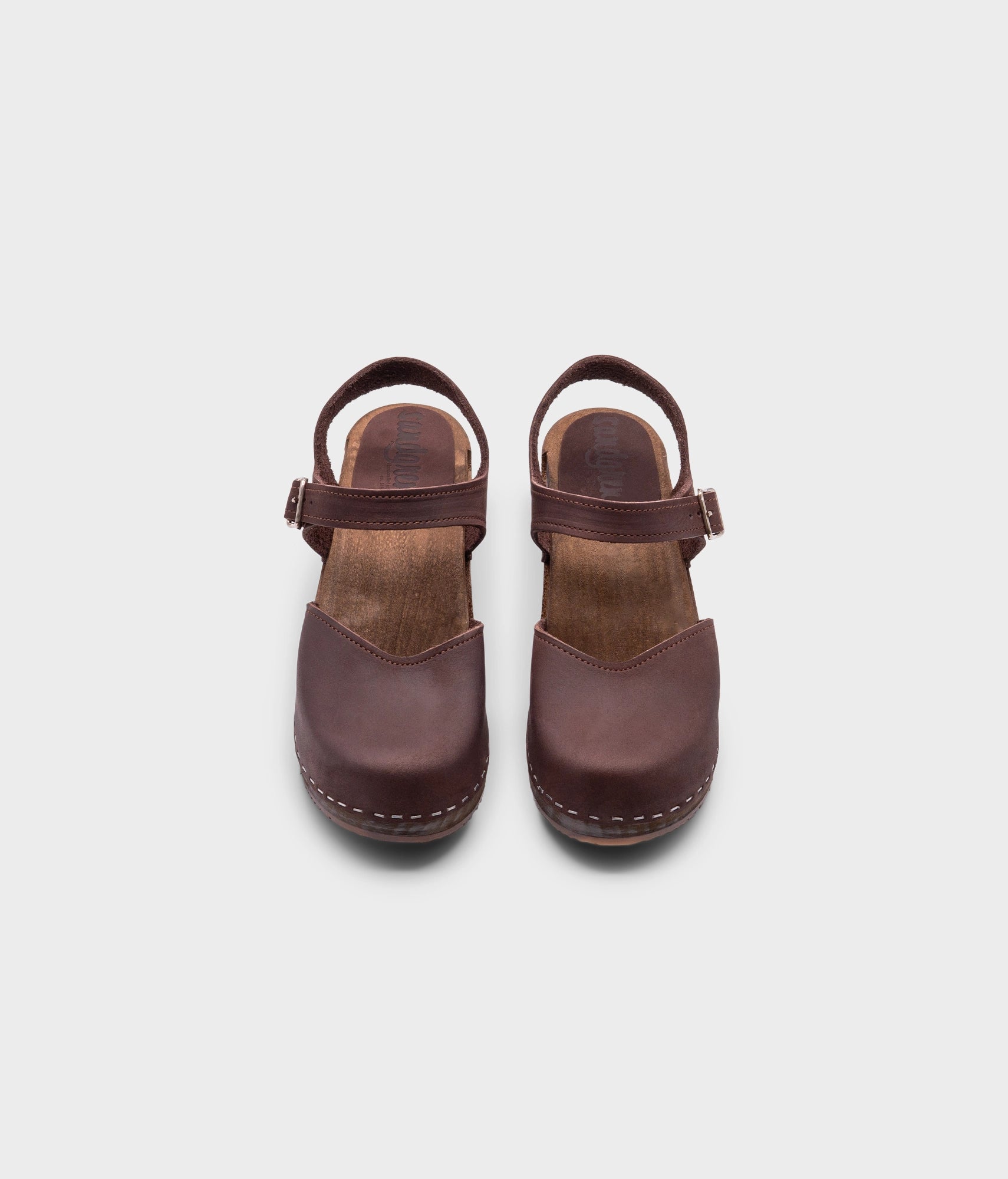 high heeled closed-toe clog sandal in dark brown nubuck leather stapled on a dark wooden base