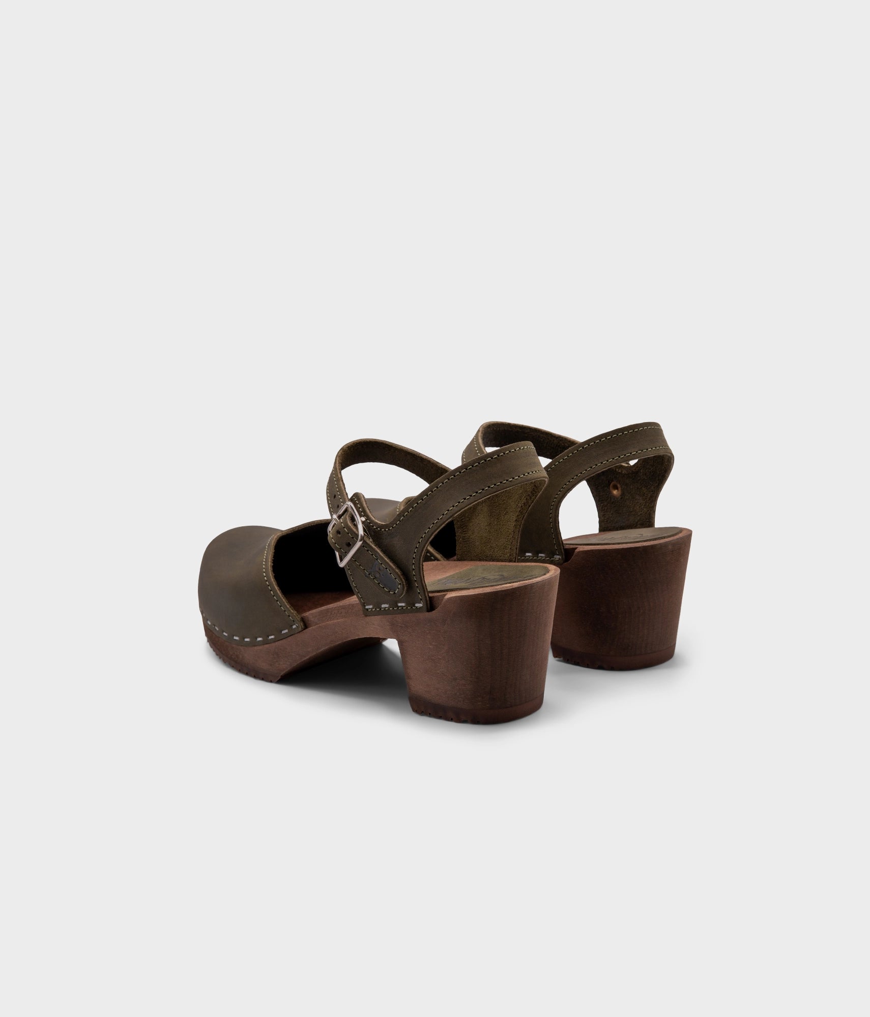 high heeled closed-toe clog sandal in olive green nubuck leather stapled on a dark wooden base
