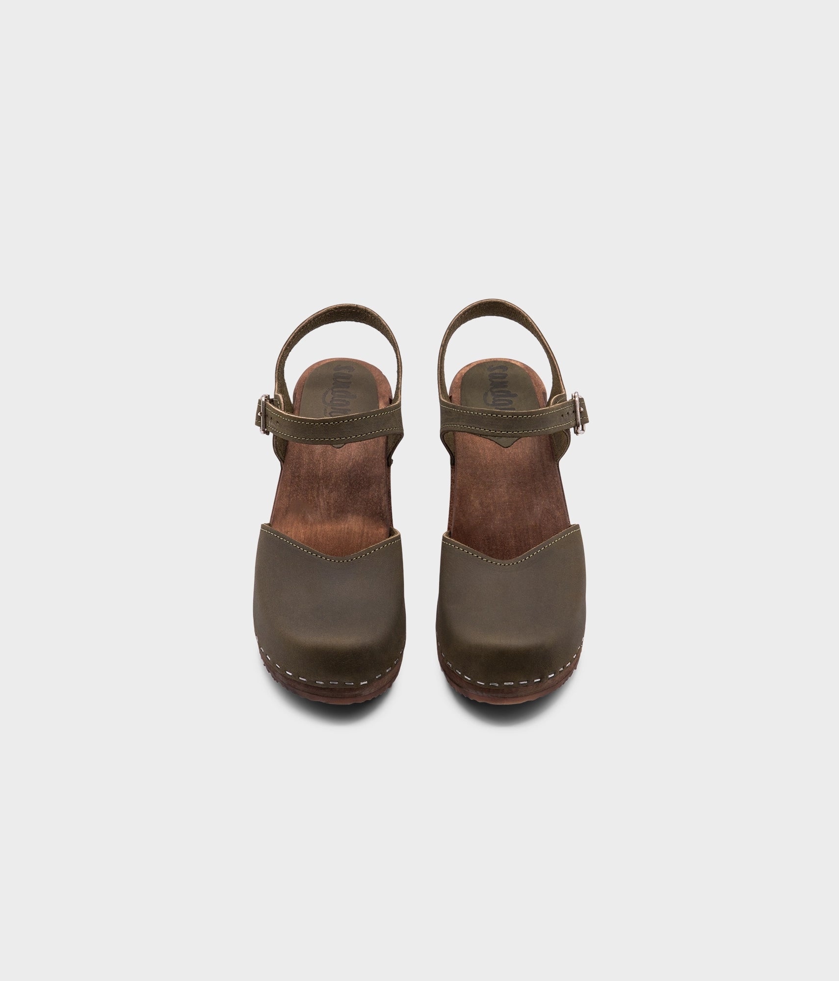 high heeled closed-toe clog sandal in olive green nubuck leather stapled on a dark wooden base