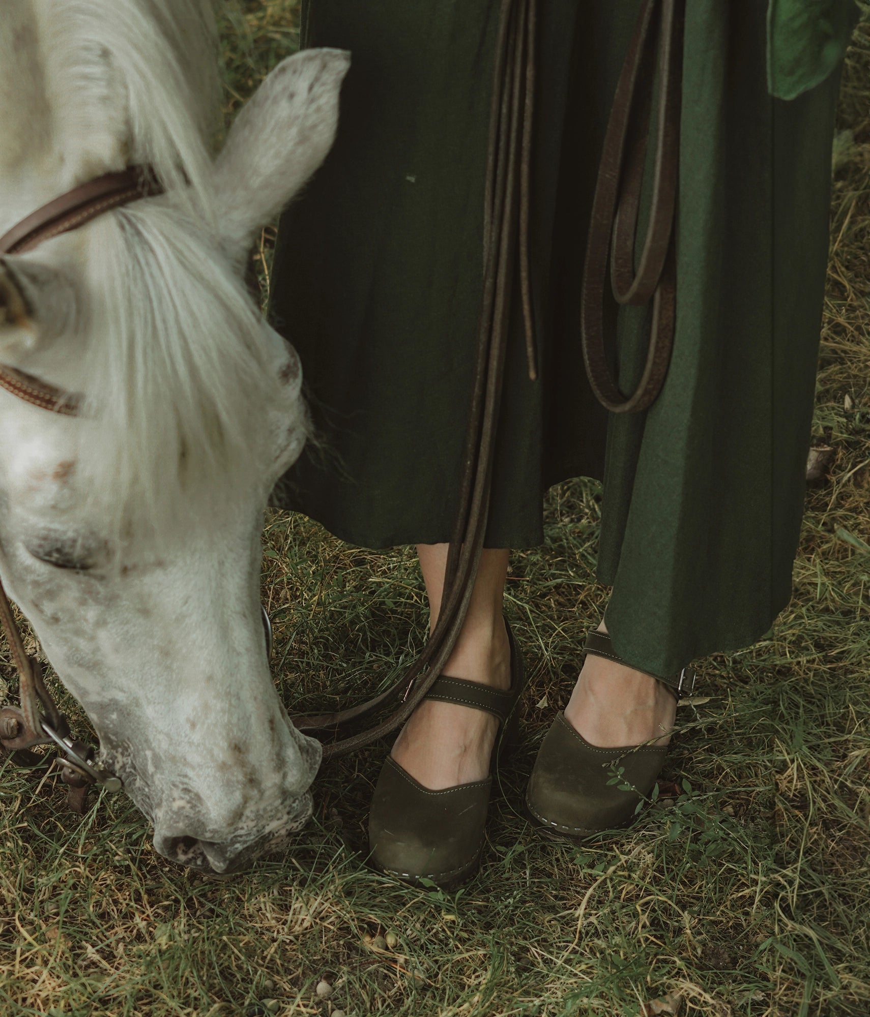 high heeled closed-toe clog sandal in olive green nubuck leather stapled on a dark wooden base