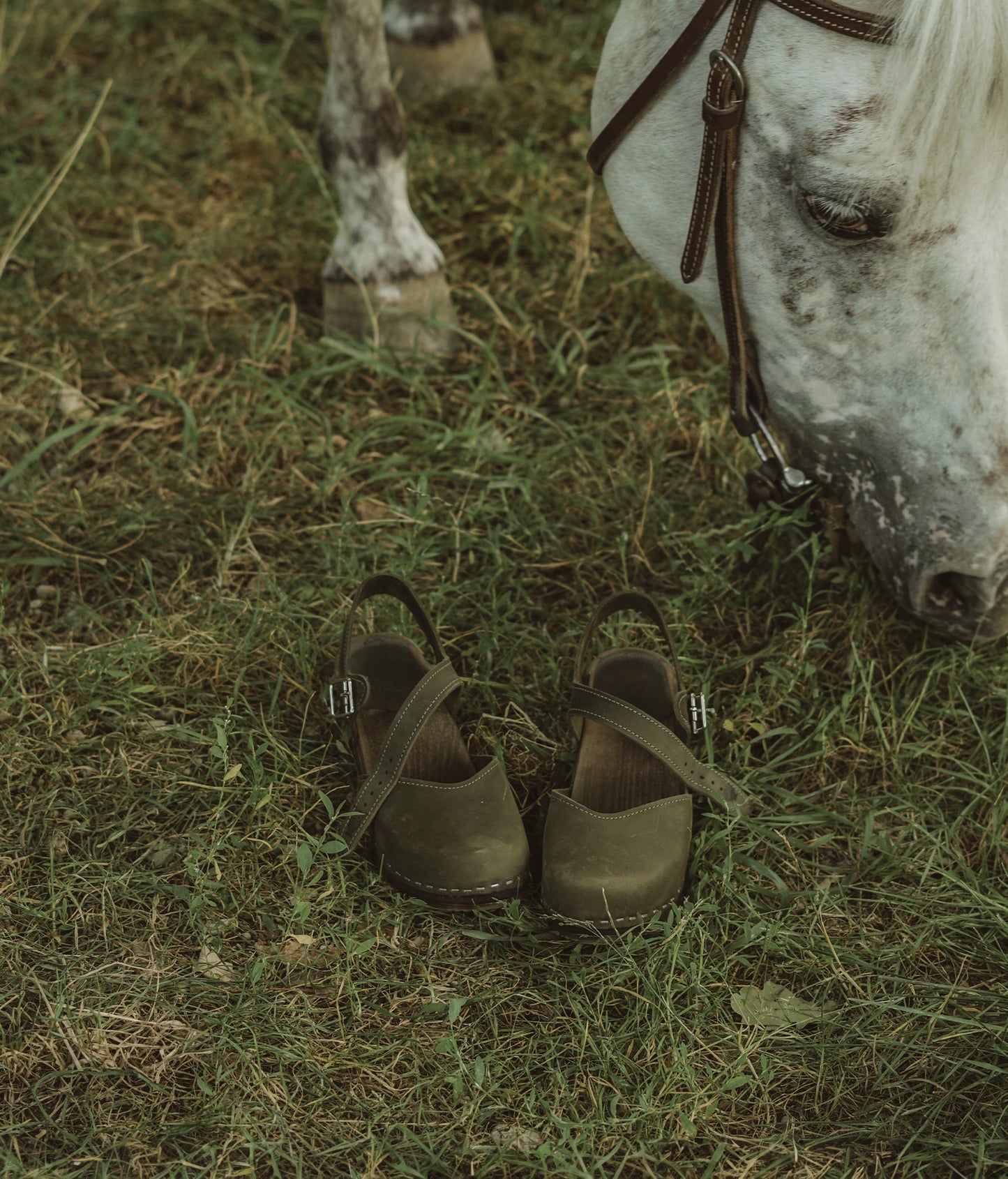 high heeled closed-toe clog sandal in olive green nubuck leather stapled on a dark wooden base
