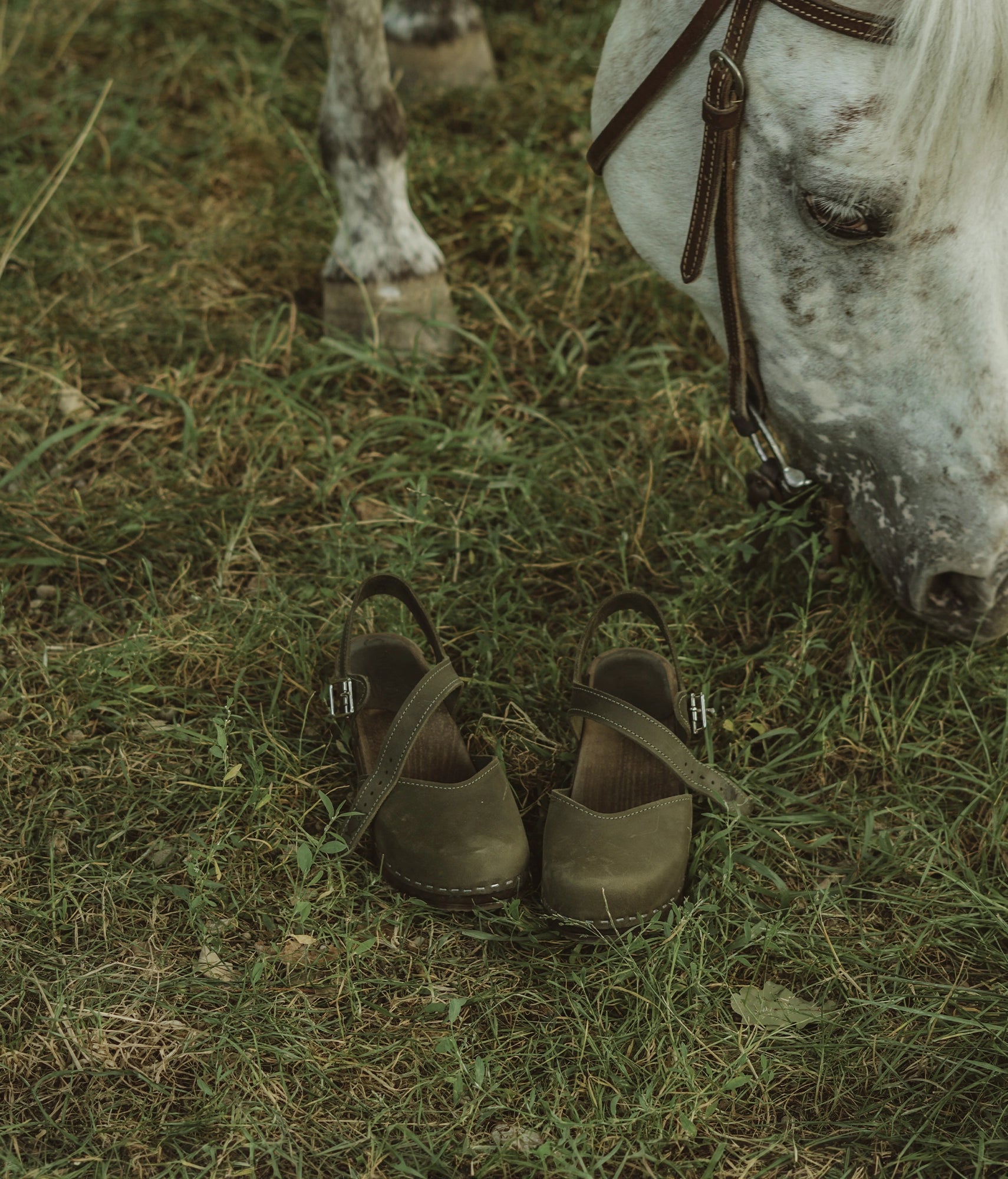 high heeled closed-toe clog sandal in olive green nubuck leather stapled on a dark wooden base