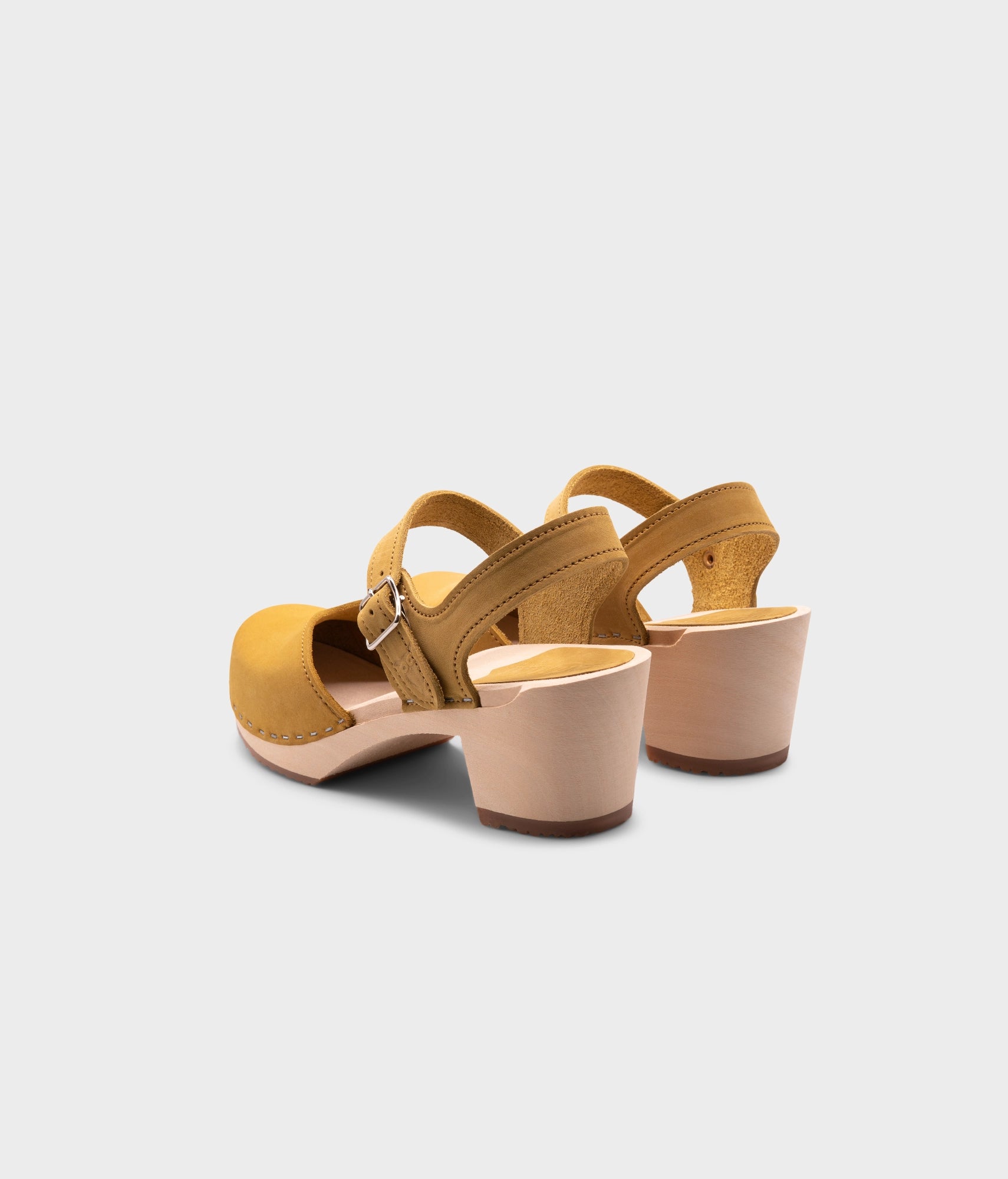 high-heeled clog sandals with a closed toe in yellow leather stapled on a light wooden base