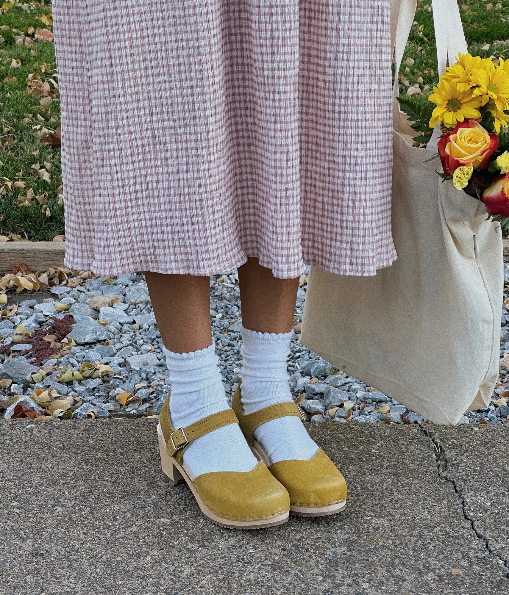 high-heeled clog sandals with a closed toe in yellow leather stapled on a light wooden base