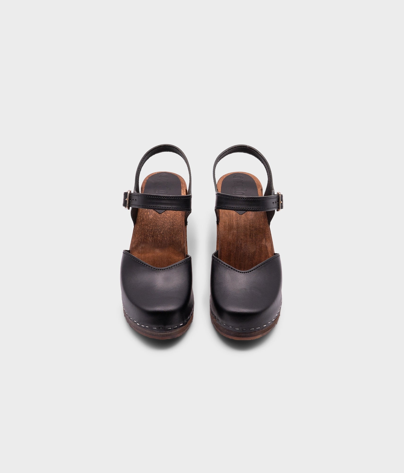 high heeled closed-toe clog sandal in black vegetable tanned leather stapled on a dark wooden base