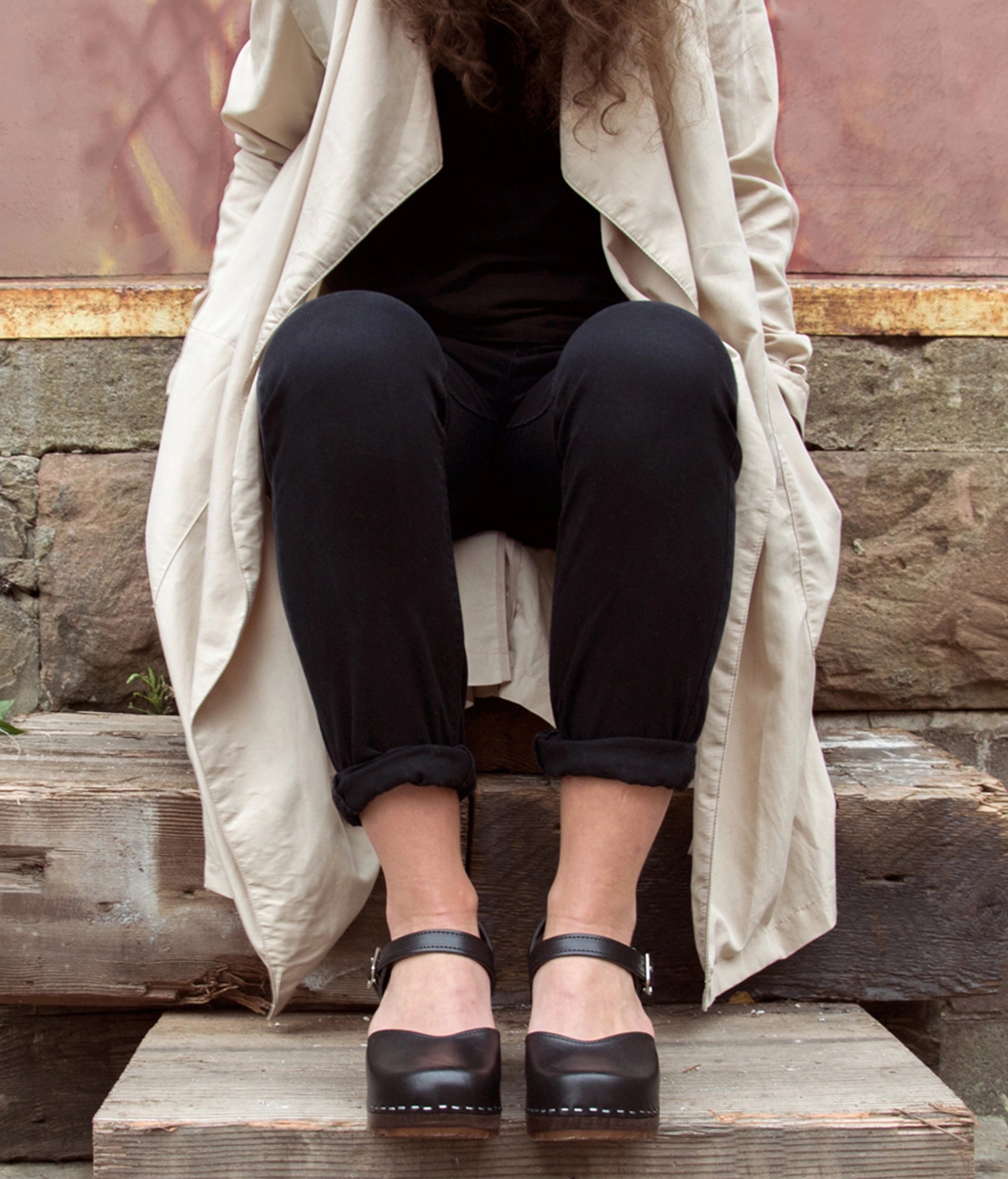 Woman wearing high heeled closed-toe clog sandal in black vegetable tanned leather stapled on a dark wooden base