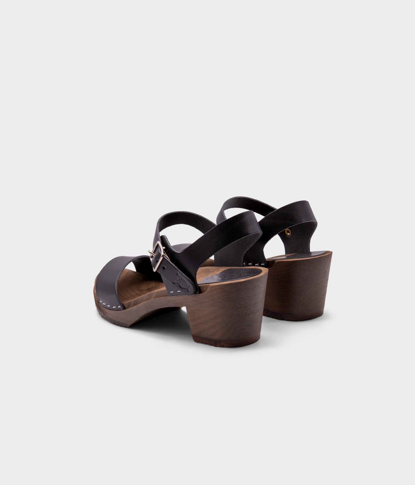 high-heeled open-toe clog sandal in black vegetable tanned leather stapled on a dark wooden base