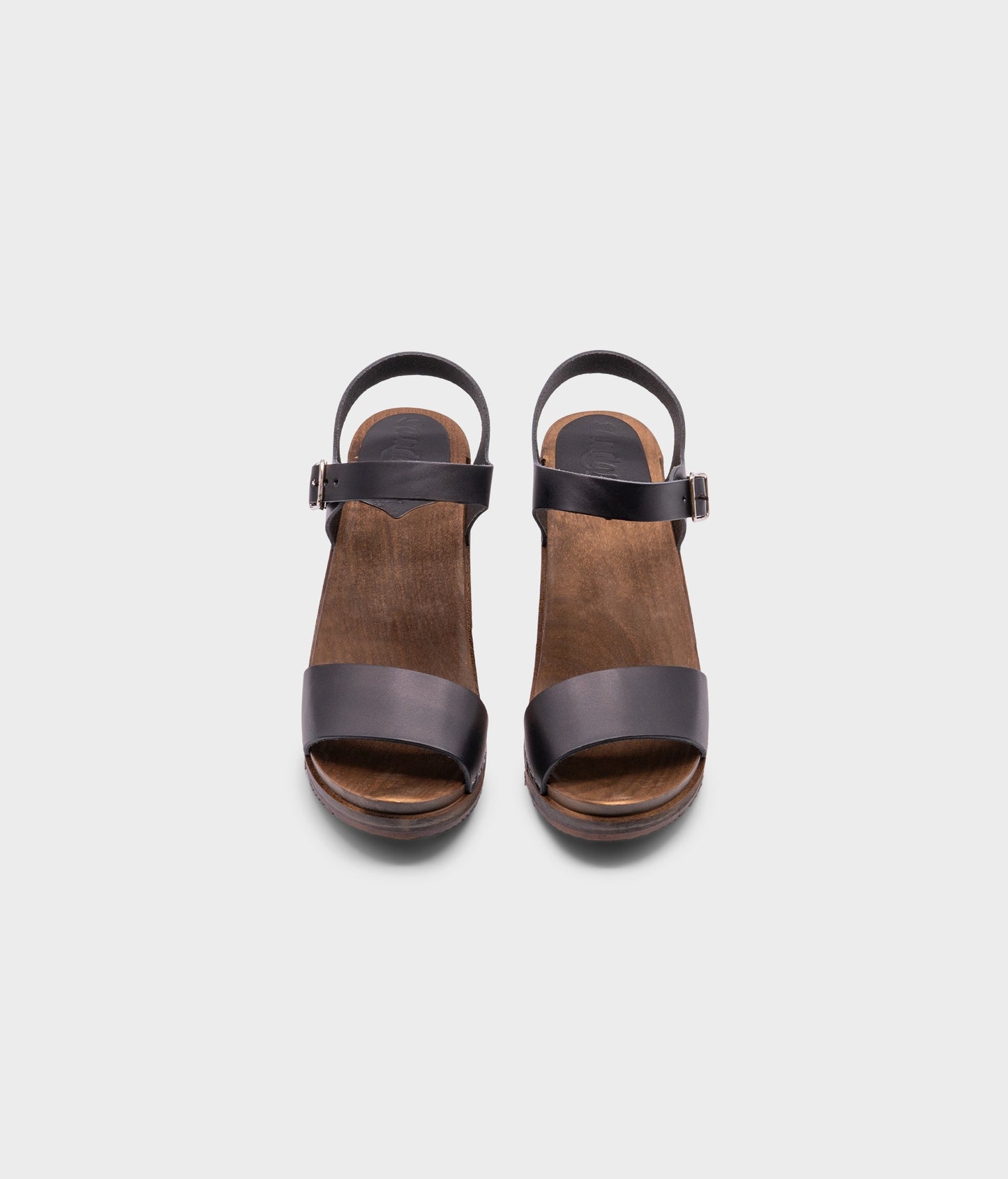 high-heeled open-toe clog sandal in black vegetable tanned leather stapled on a dark wooden base