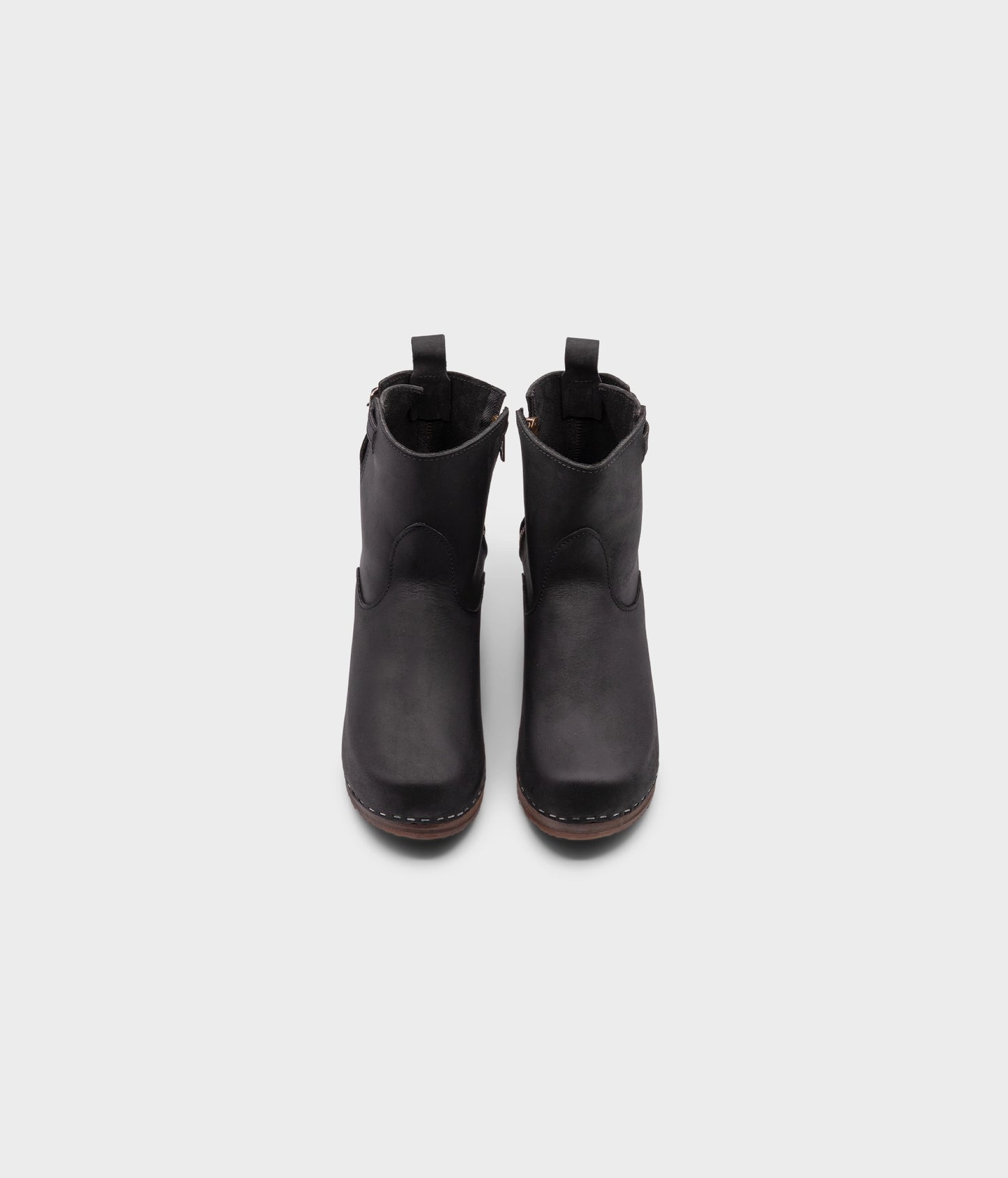 high-heeled clog boots in black nubuck leather stapled on a dark wooden base with a silver buckle