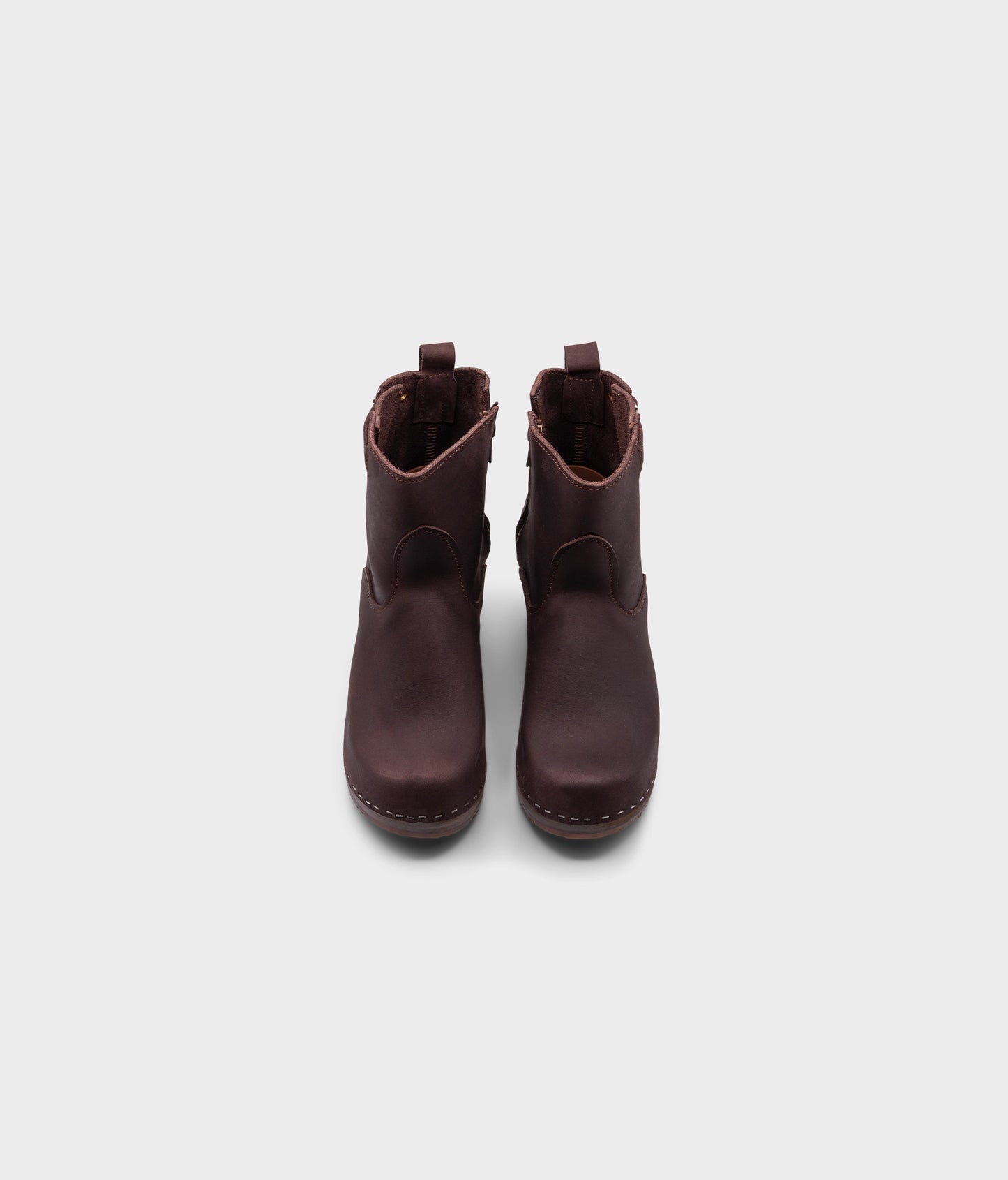 high-heeled clog boots in dark brown nubuck leather stapled on a dark wooden base with a silver buckle