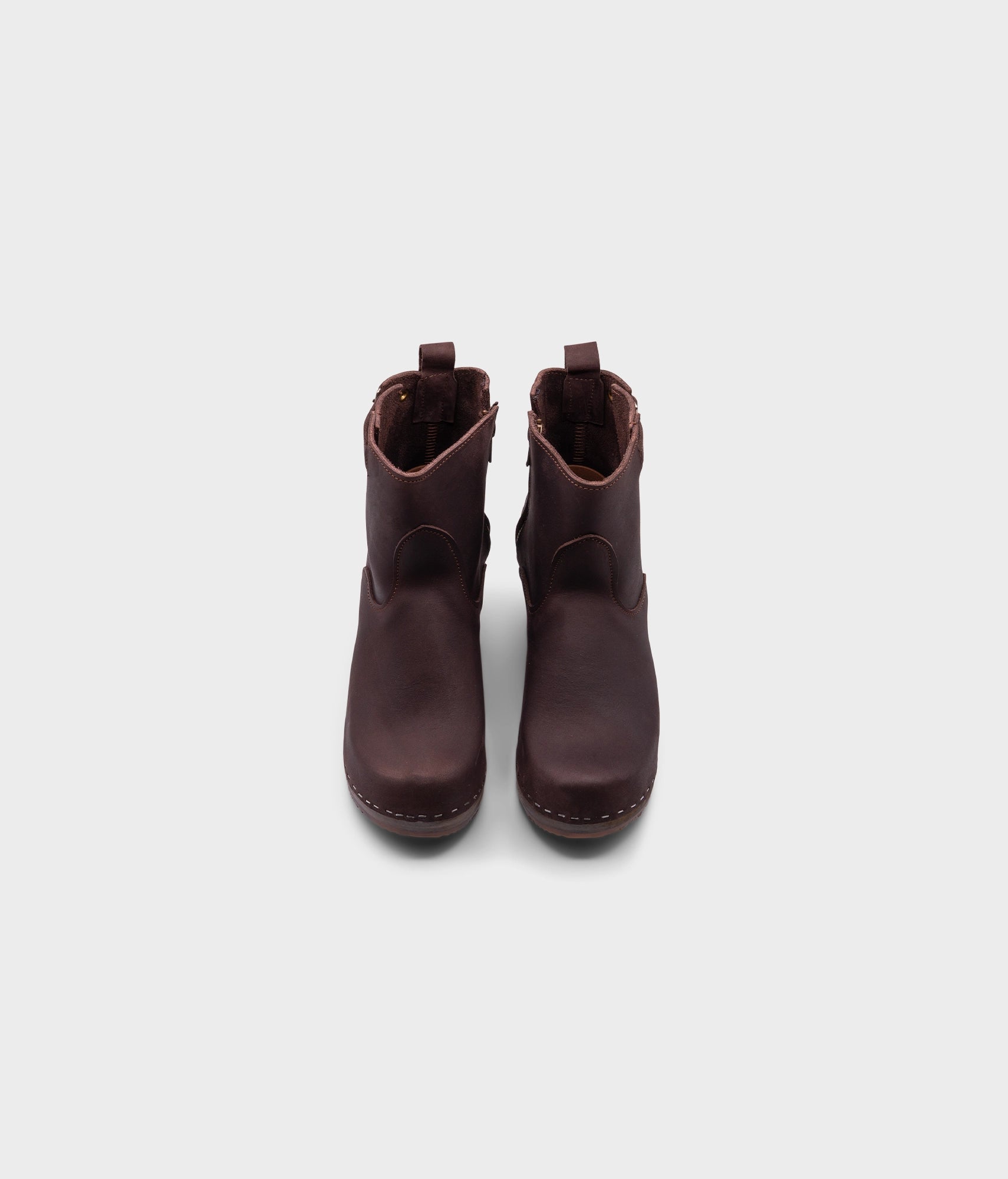 high-heeled clog boots in dark brown nubuck leather stapled on a dark wooden base with a silver buckle
