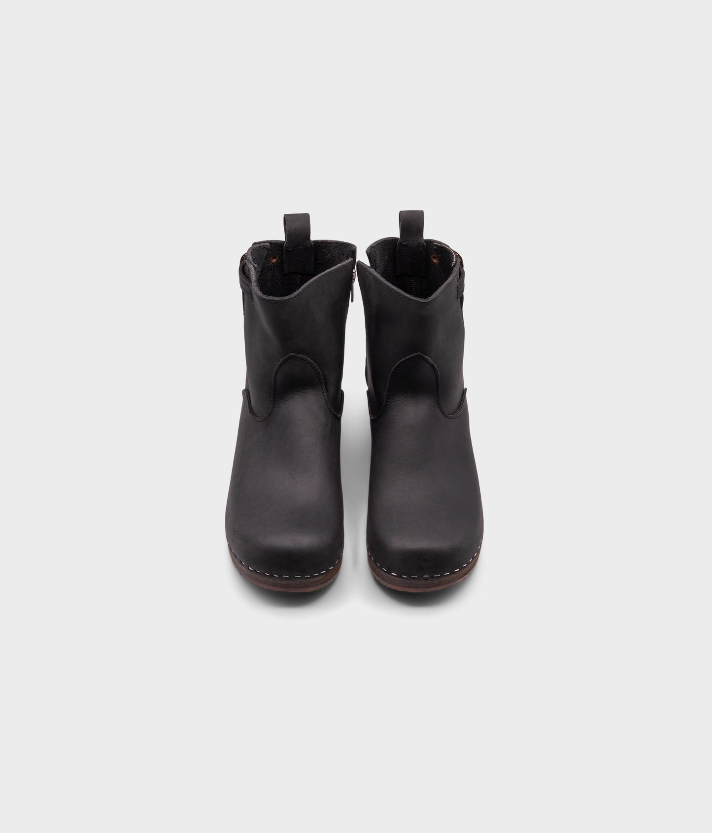low heeled clog boots in black nubuck leather with a mid-shaft and silver buckle, stapled on a dark wooden base
