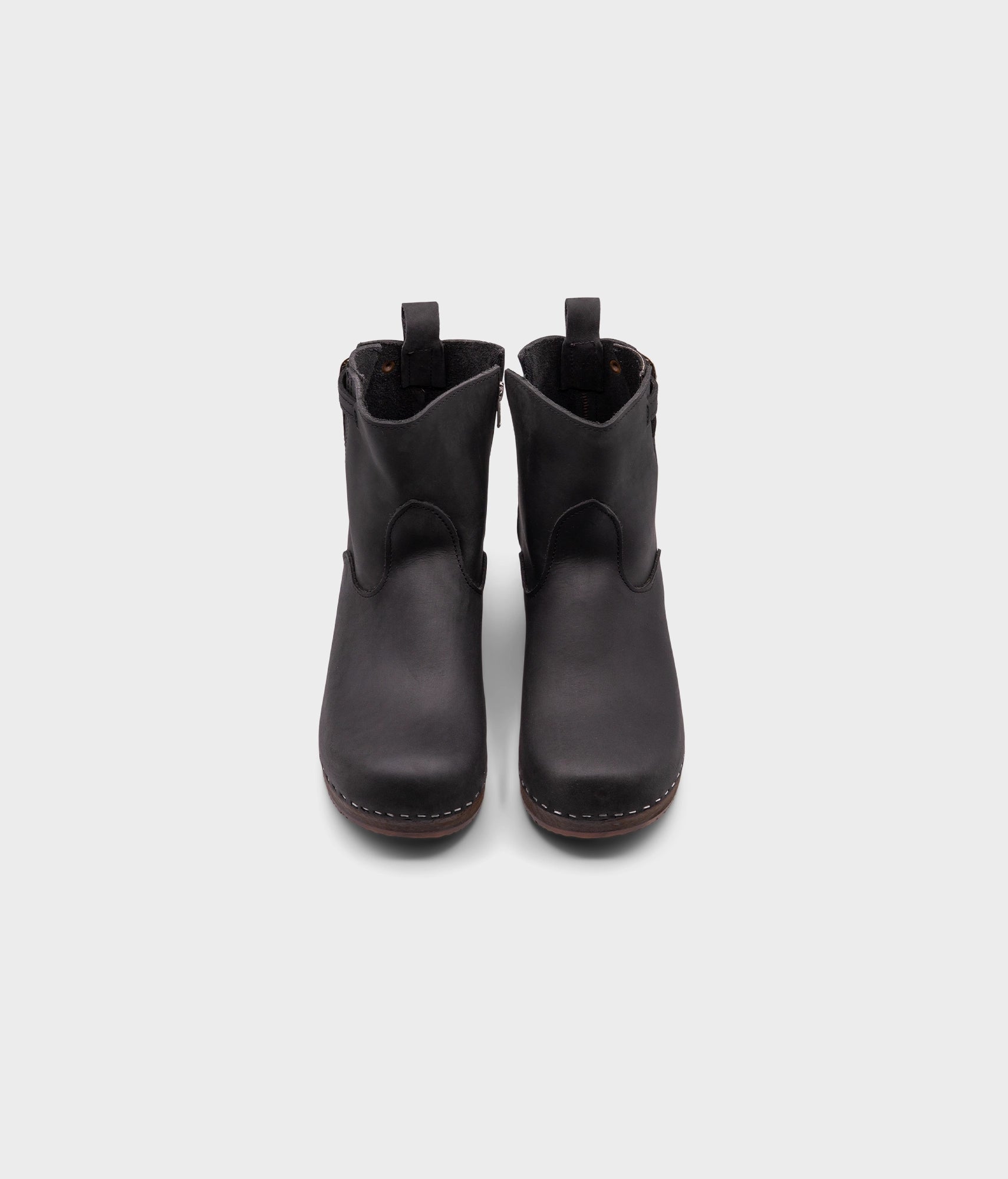 low heeled clog boots in black nubuck leather with a mid-shaft and silver buckle, stapled on a dark wooden base