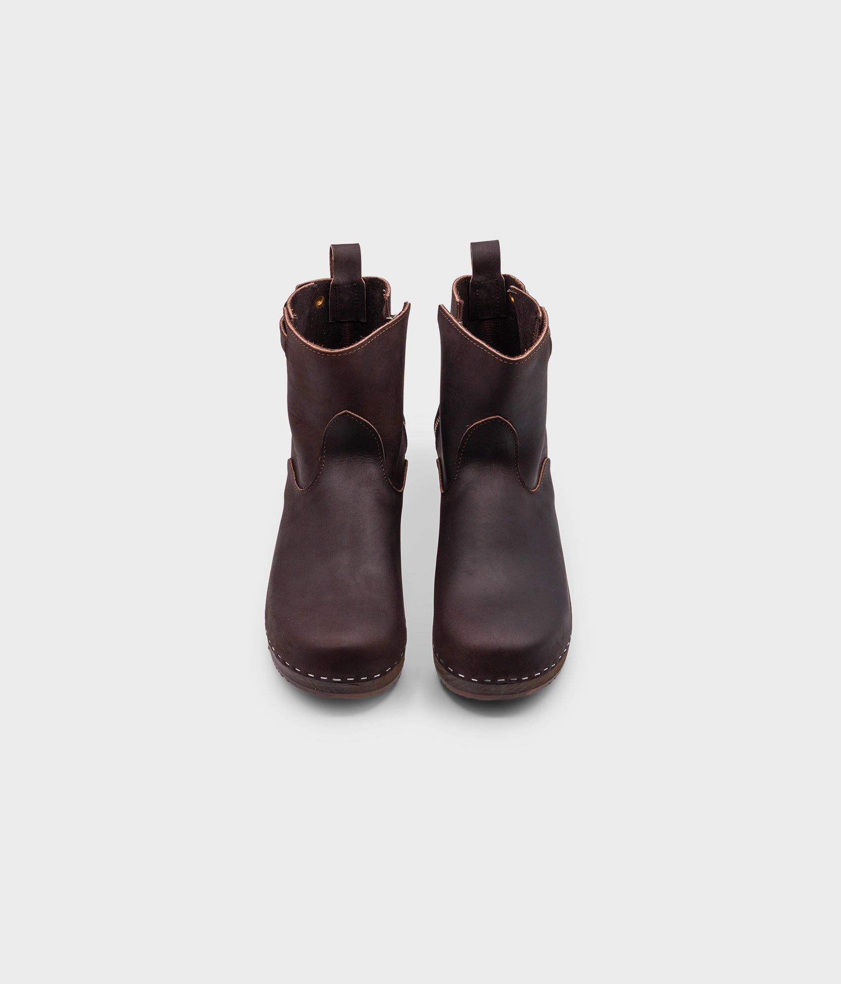 low heeled clog boots in dark brown nubuck leather with a mid-shaft and silver buckle, stapled on a dark wooden base