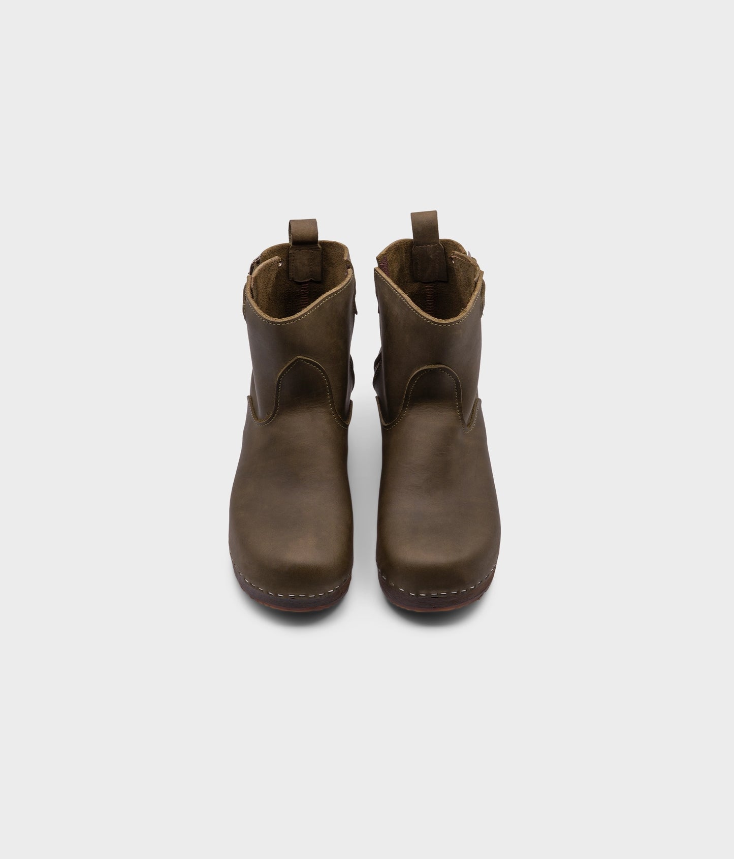 low heeled clog boots in olive green nubuck leather with a mid-shaft and silver buckle, stapled on a dark wooden base