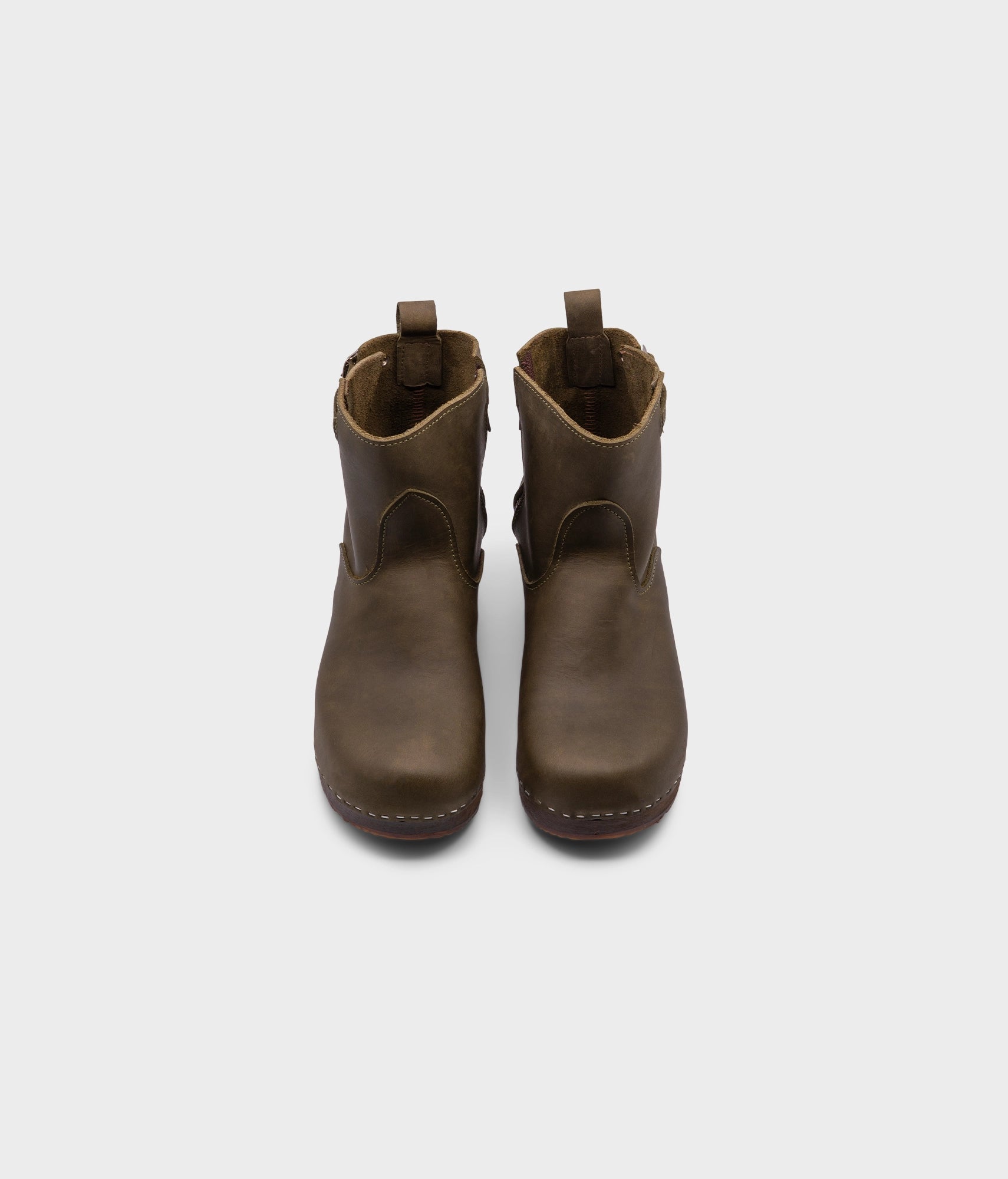 low heeled clog boots in olive green nubuck leather with a mid-shaft and silver buckle, stapled on a dark wooden base