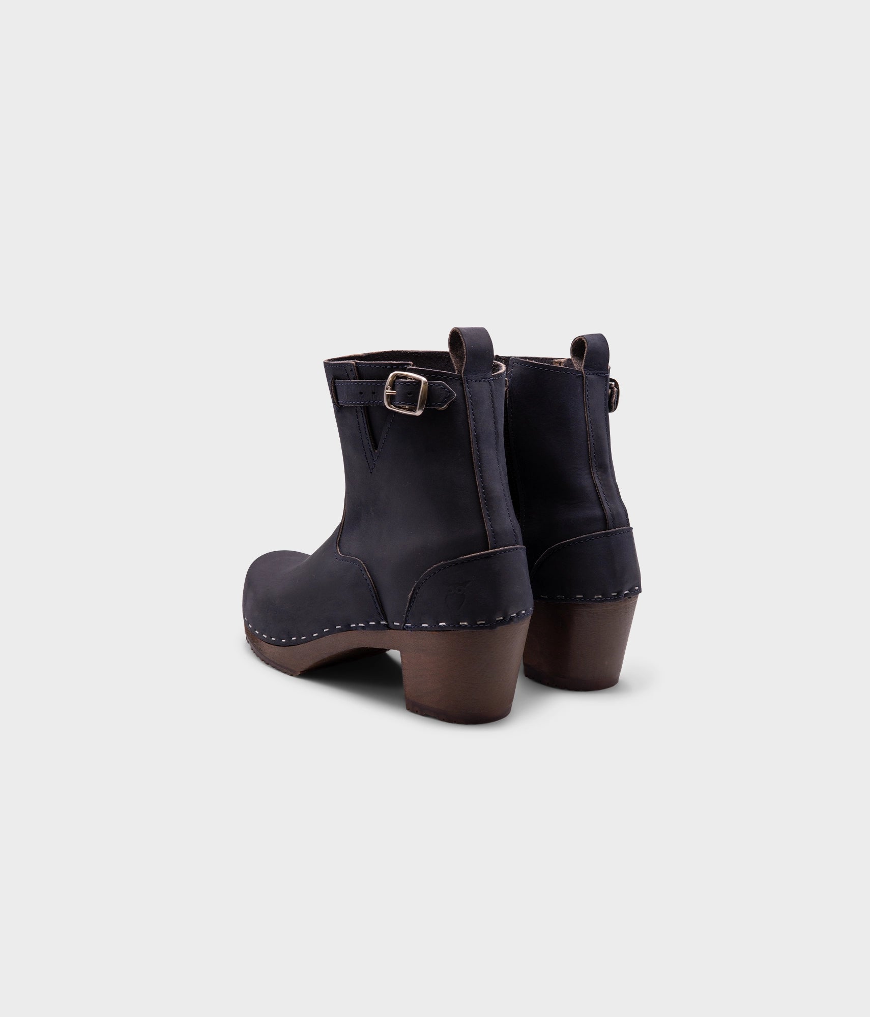 high-heeled clog boots in navy blue nubuck leather stapled on a dark wooden base with a silver buckle