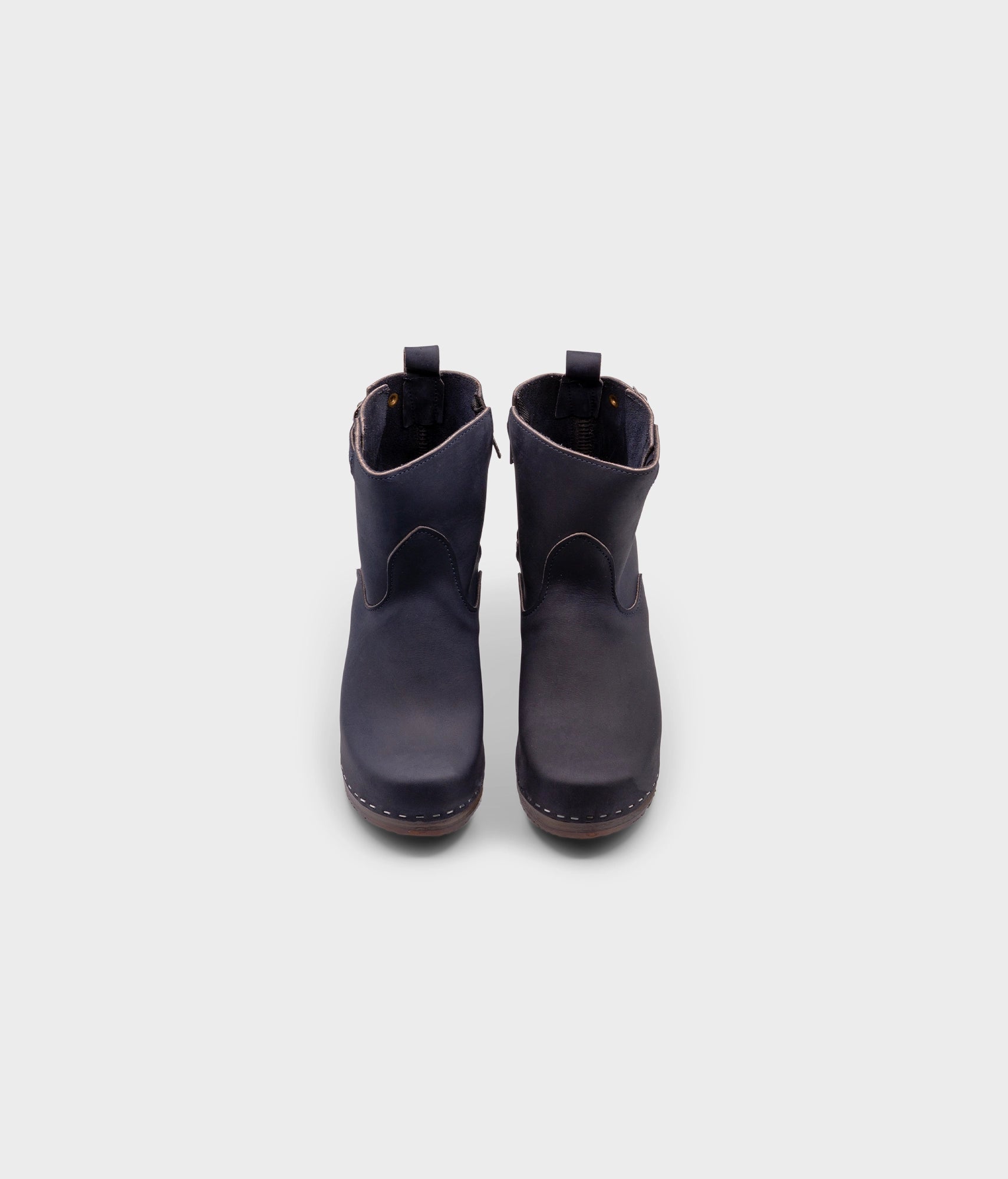 high-heeled clog boots in navy blue nubuck leather stapled on a dark wooden base with a silver buckle