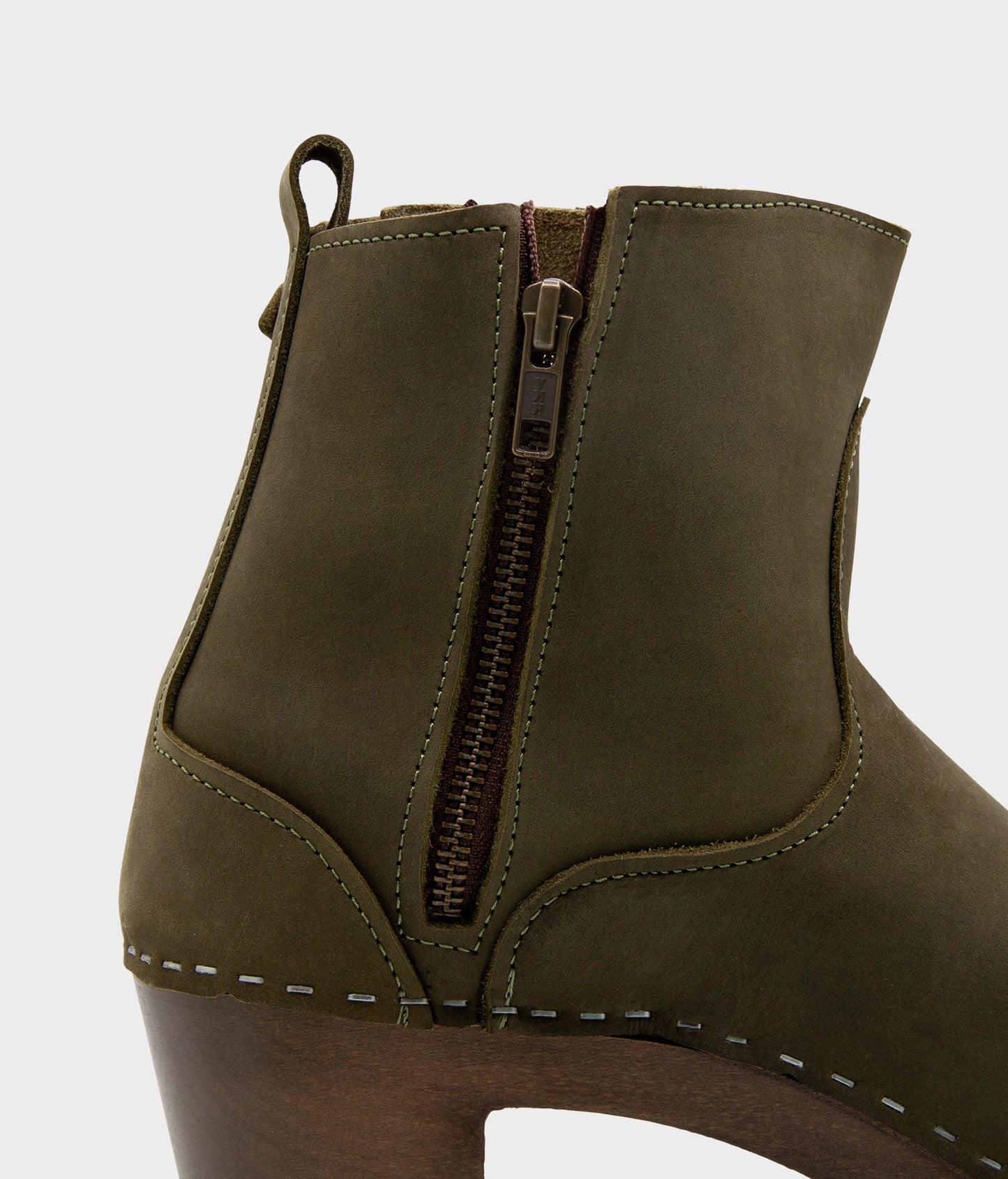 high-heeled clog boots in olive green nubuck leather stapled on a dark wooden base with a silver buckle