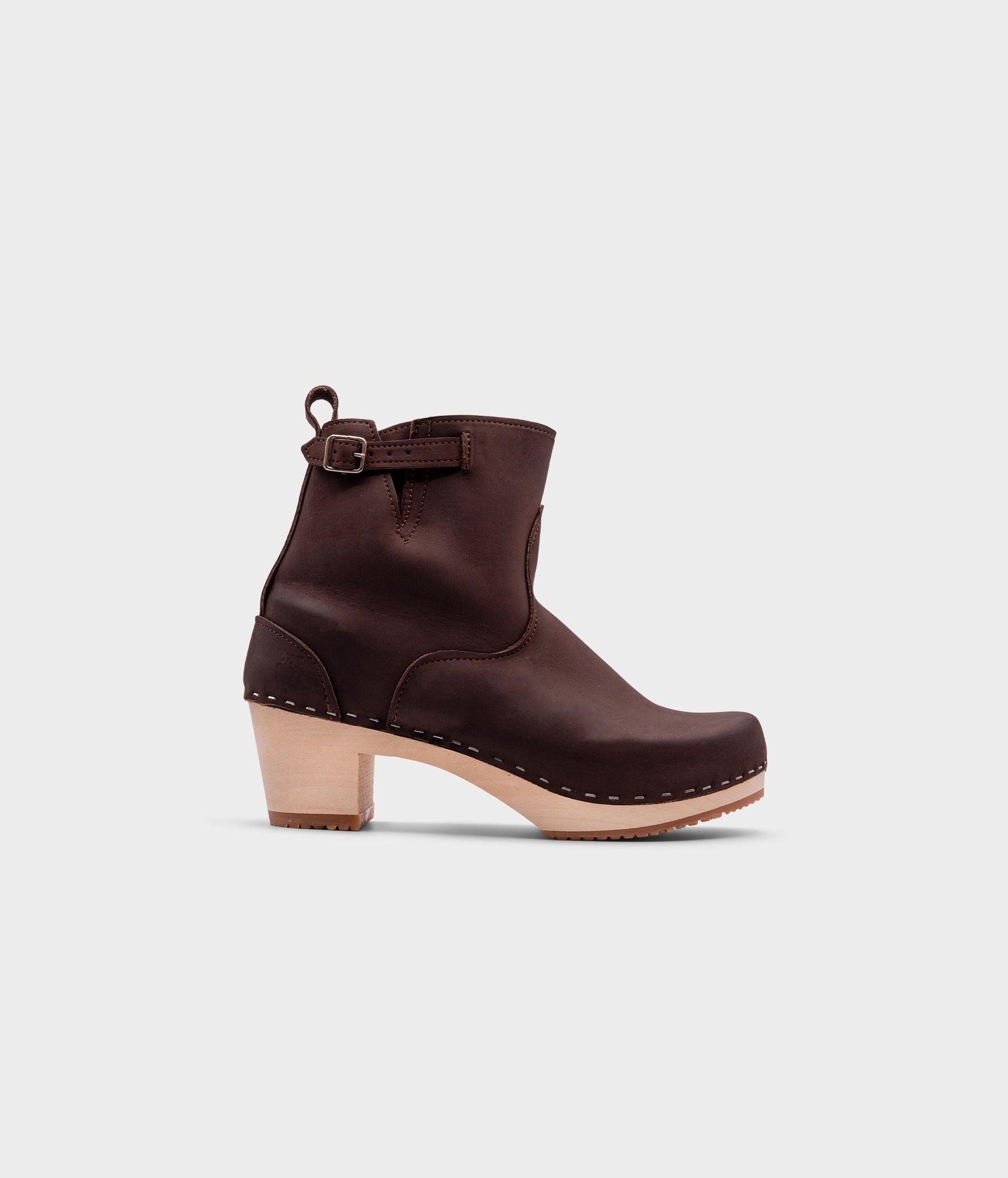 high-heeled clog boots in dark brown nubuck leather stapled on a light wooden base with a silver buckle