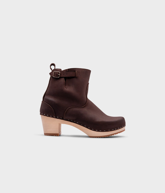 high-heeled clog boots in dark brown nubuck leather stapled on a light wooden base with a silver buckle