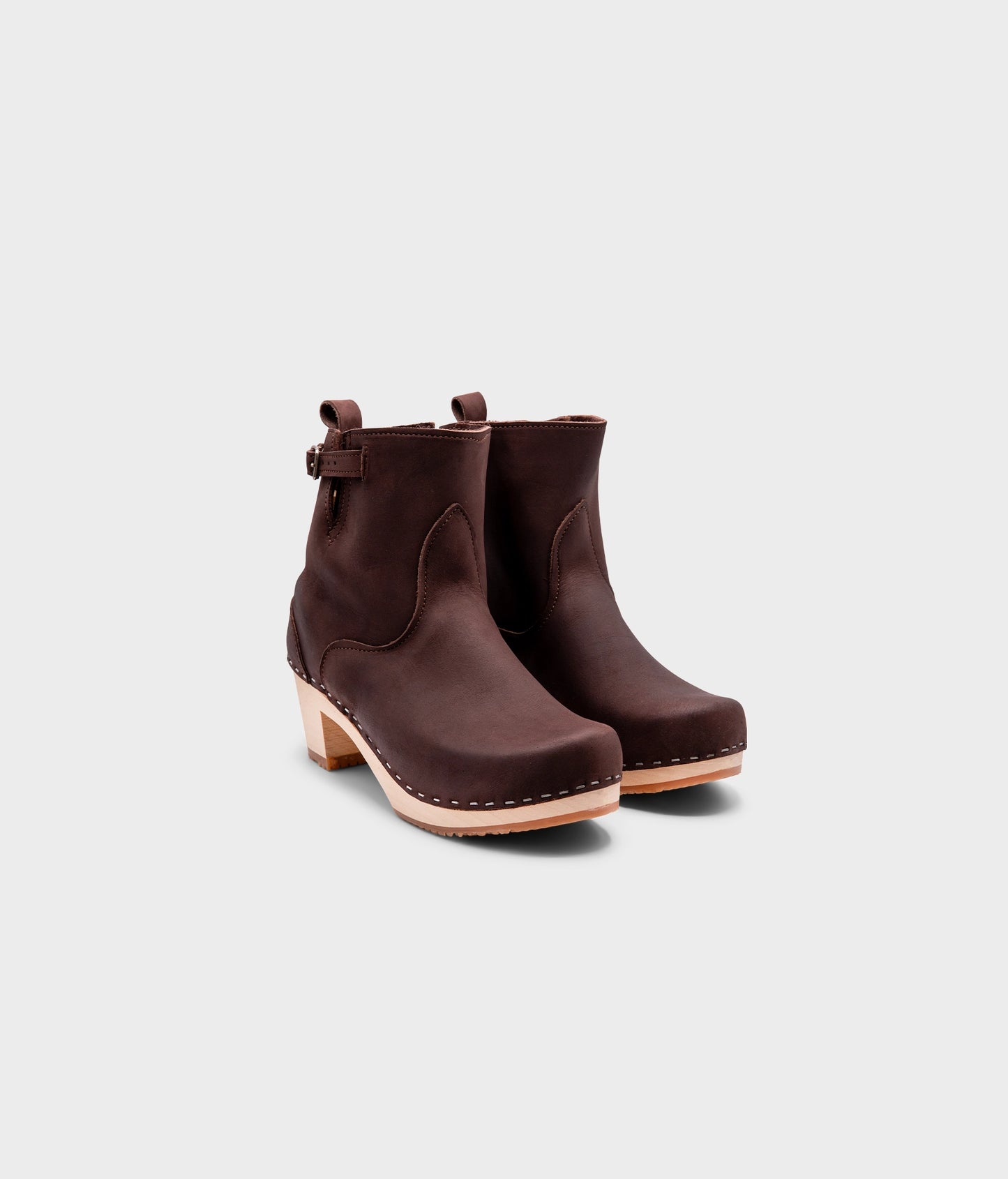 high-heeled clog boots in dark brown nubuck leather stapled on a light wooden base with a silver buckle