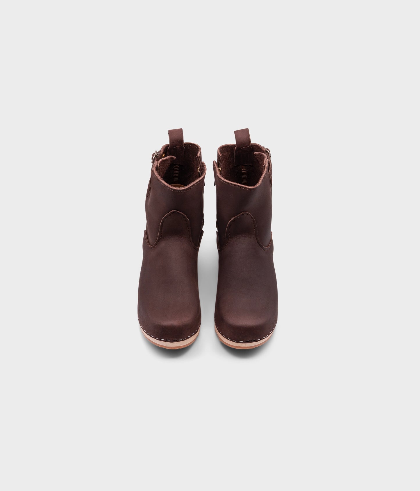 high-heeled clog boots in dark brown nubuck leather stapled on a light wooden base with a silver buckle