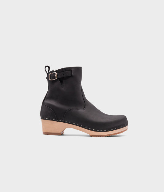 low-heeled clog boots in black nubuck  leather stapled on a light wooden base
