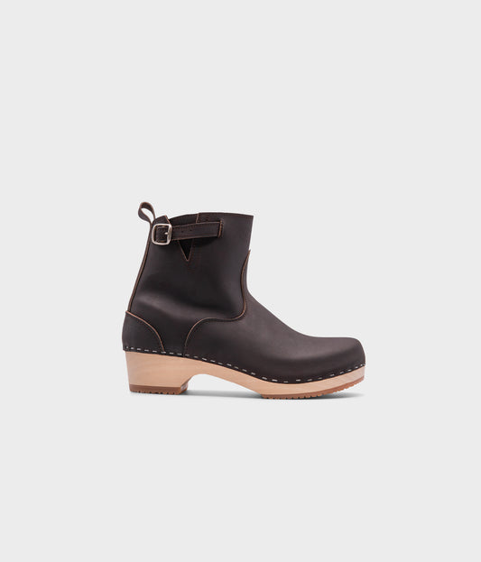 low-heeled clog boots in dark brown leather stapled on a light wooden base