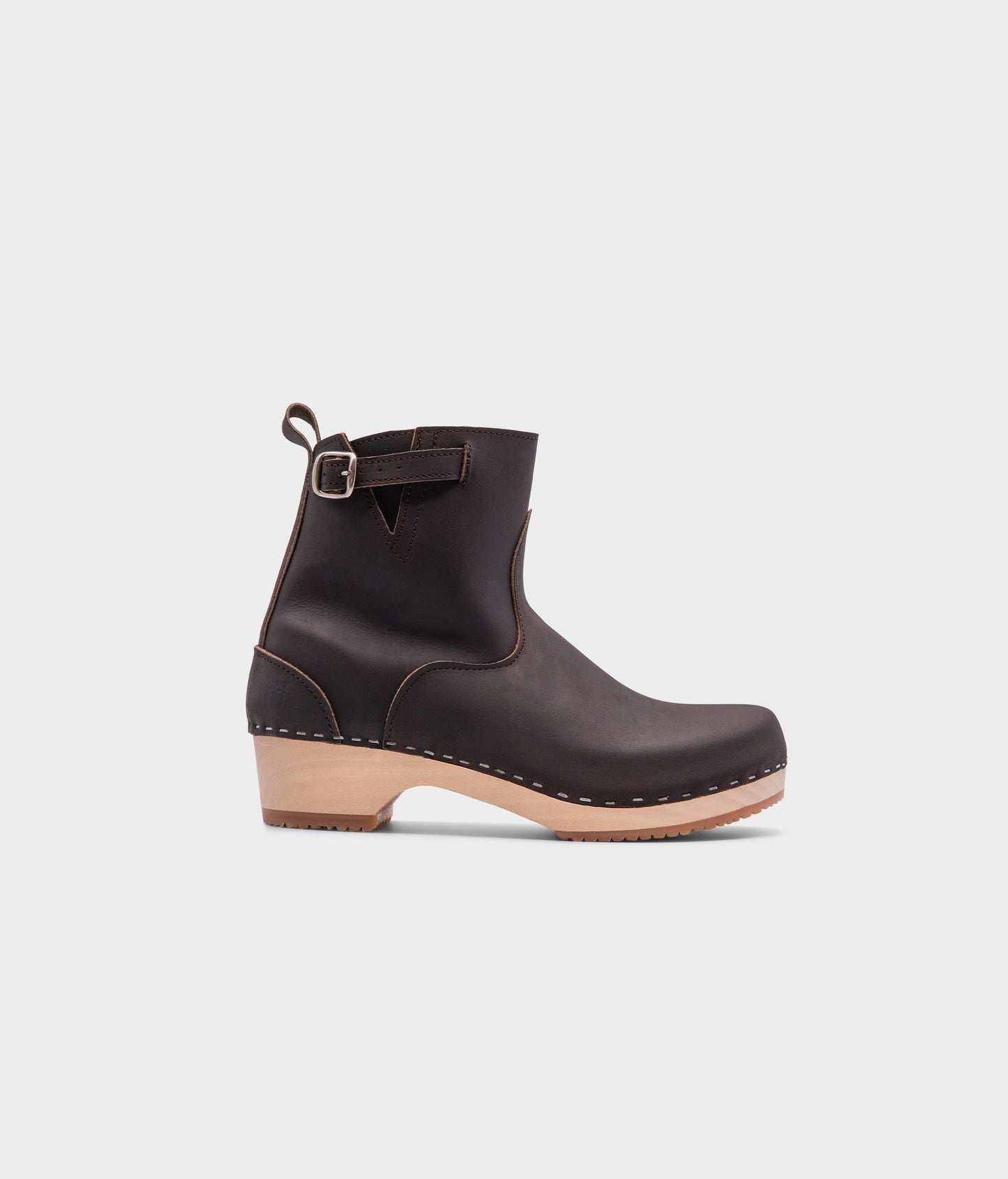 low-heeled clog boots in dark brown leather stapled on a light wooden base