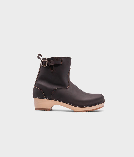 low-heeled clog boots in dark brown leather stapled on a light wooden base