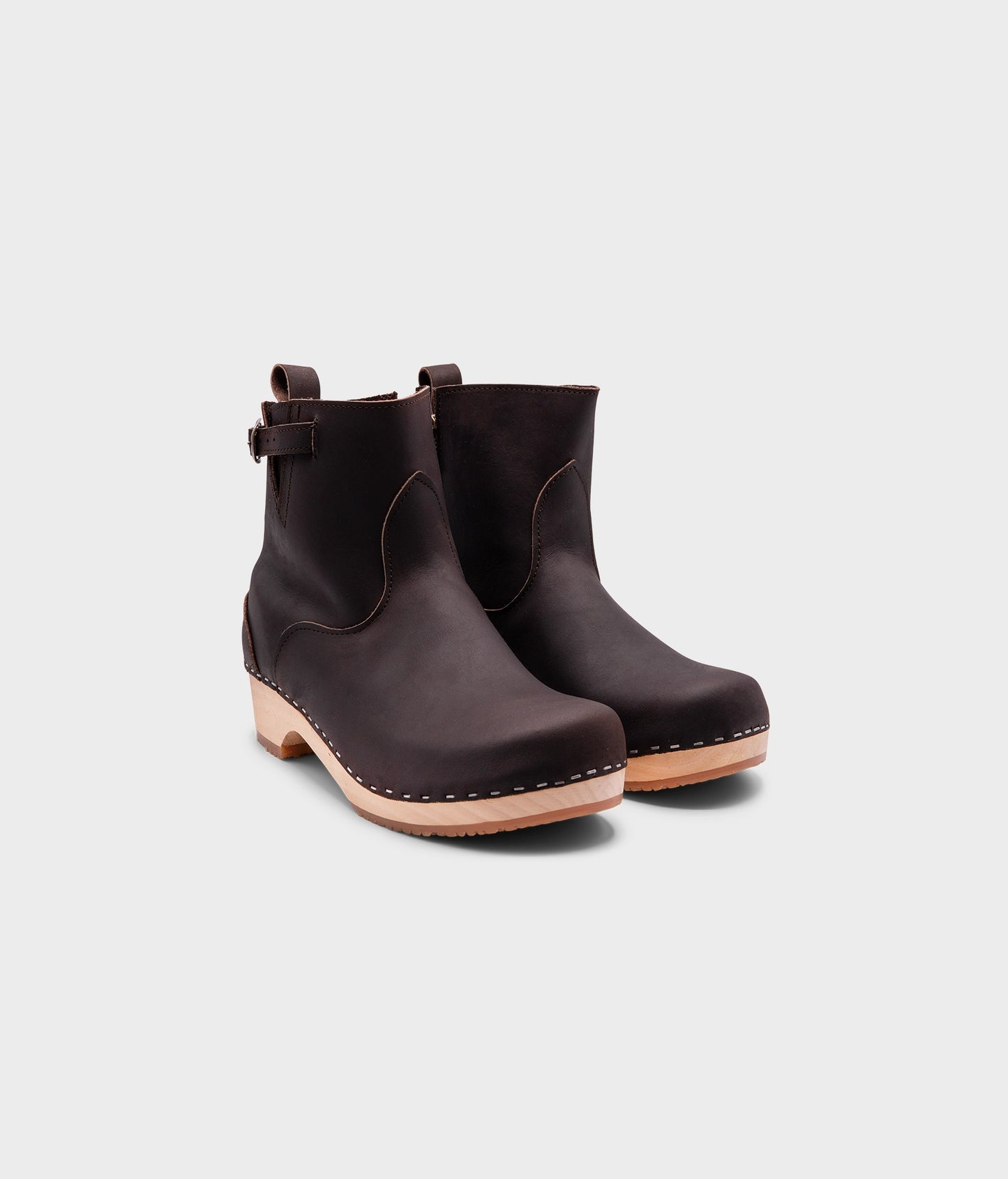 low-heeled clog boots in dark brown leather stapled on a light wooden base