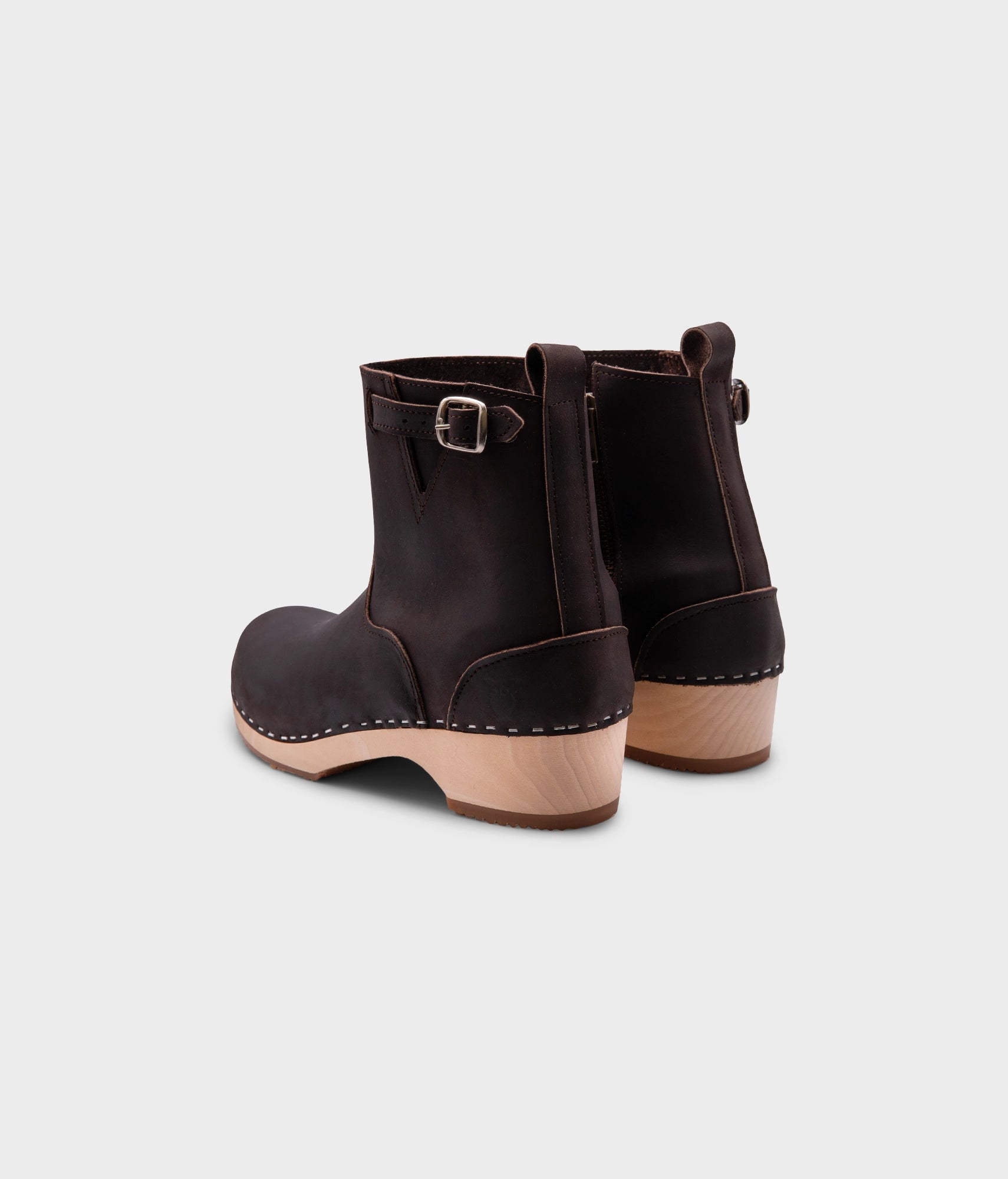 low-heeled clog boots in dark brown leather stapled on a light wooden base